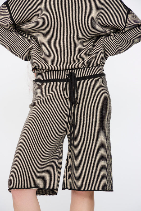 Person wearing Lauren Manoogian's Linea Shorts in Black Melange and Sisal with a matching relaxed fit, vertically striped black and beige pima cotton top, standing against a plain white background.