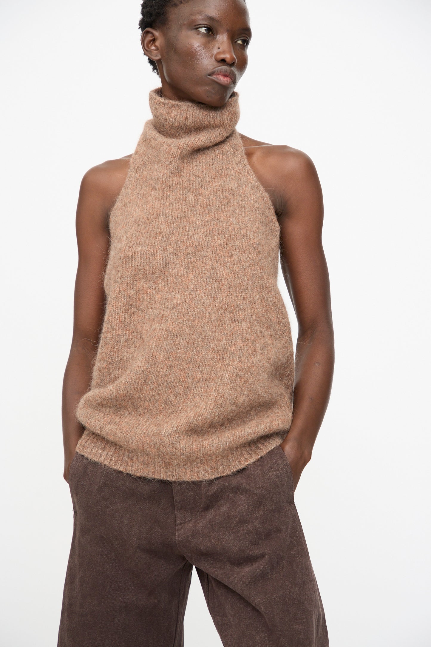 A person wears the Lauren Manoogian Loft Halter in Spice with brown pants, standing against a plain white background with hands in pockets.