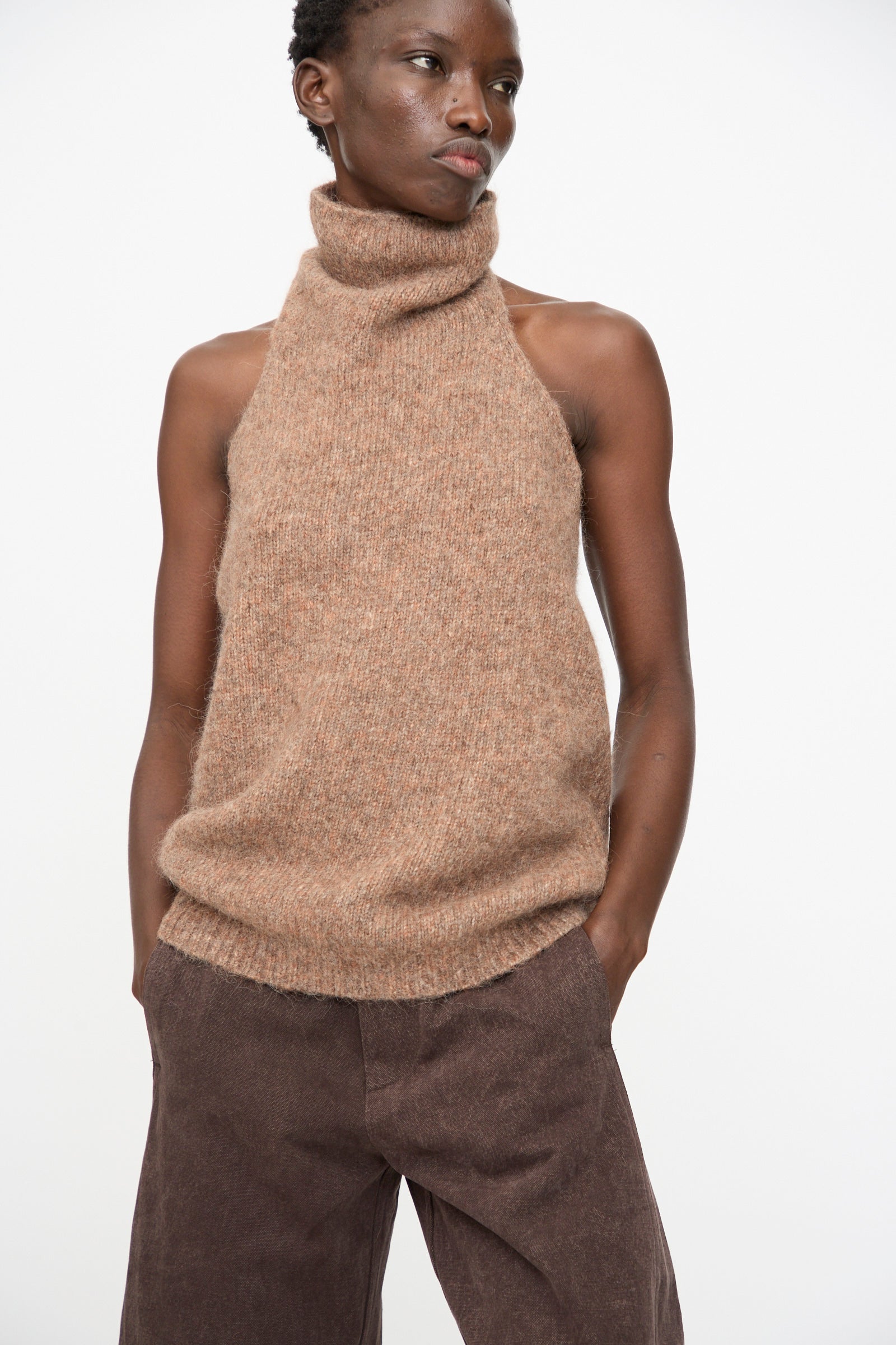 A person wears the Lauren Manoogian Loft Halter in Spice with brown pants, standing against a plain white background with hands in pockets.
