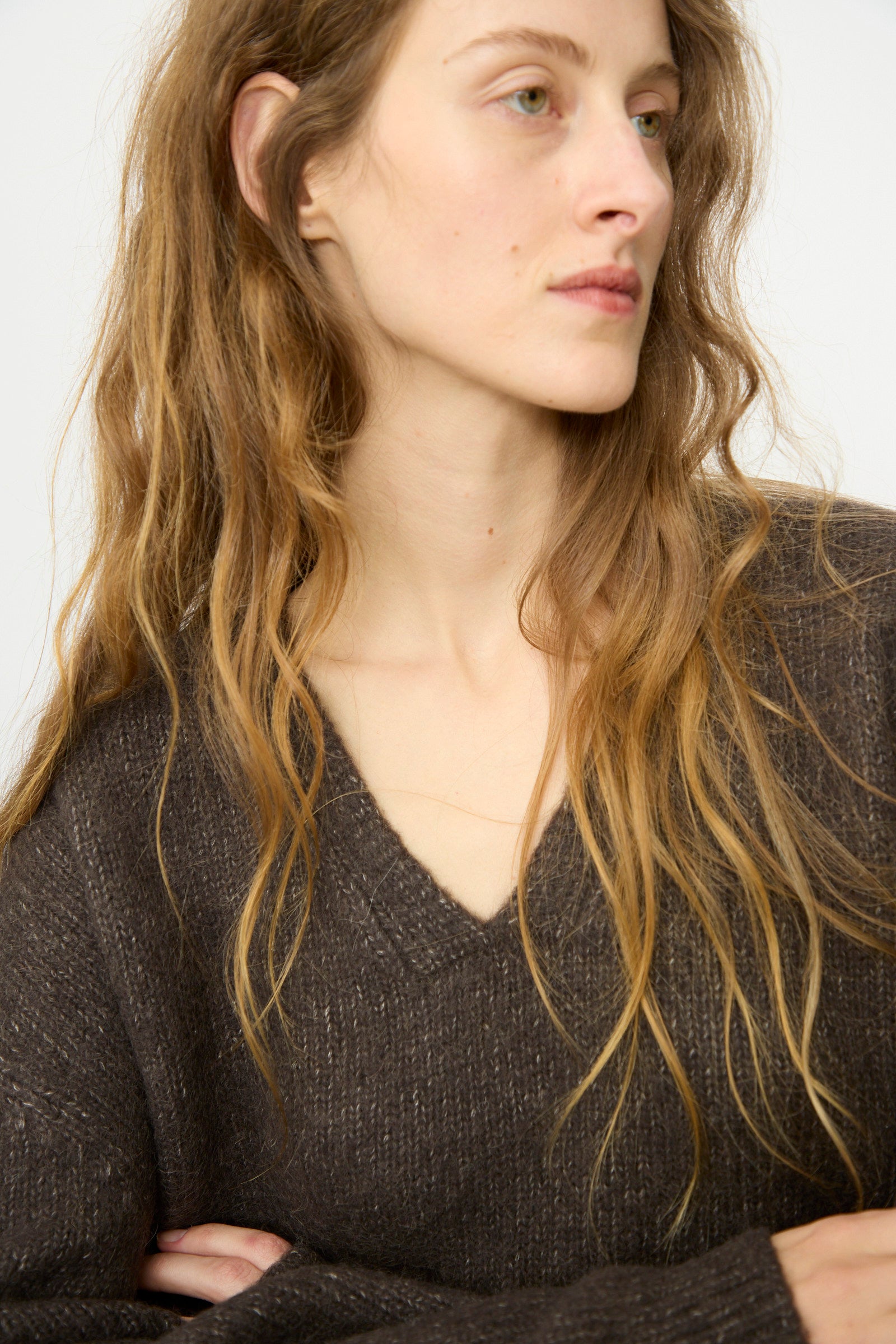 A woman with wavy light brown hair wears the Lauren Manoogian Loft V Neck in Coal, looking to the side with a neutral expression.