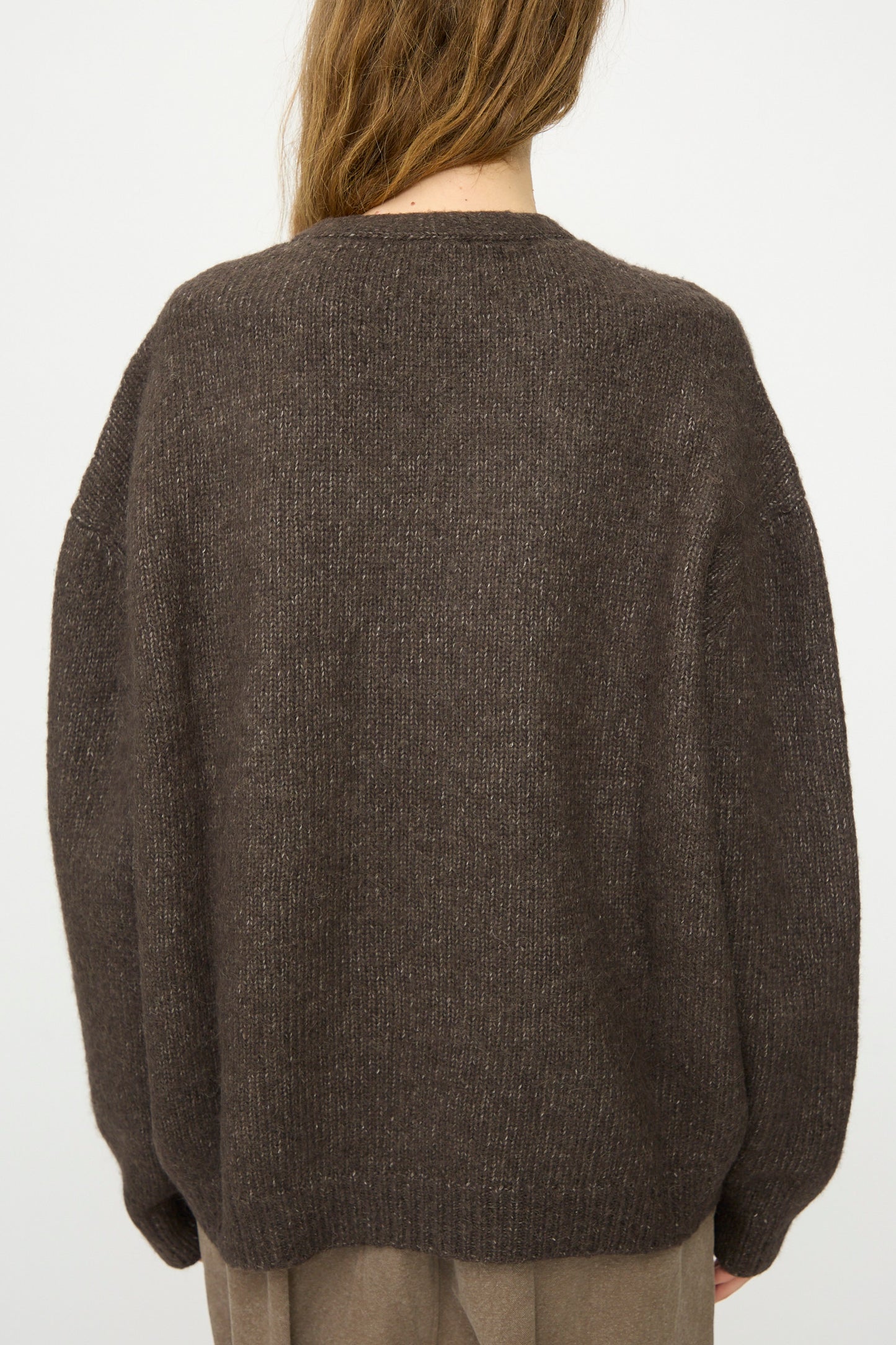 Person with long hair wearing a relaxed fit Lauren Manoogian Loft V Neck sweater in Coal and taupe pants, shown from the back against a plain white background.