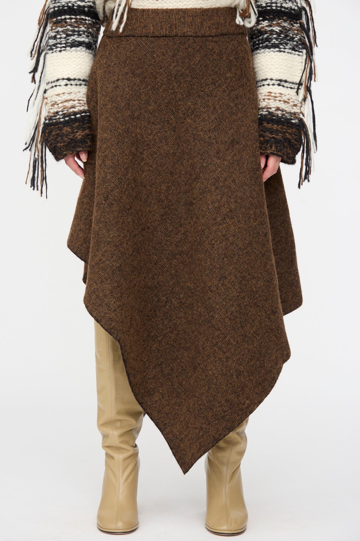 Asymmetrical brown merino wool Manta Skirt in Rust Marl by Lauren Manoogian worn over beige leather boots.