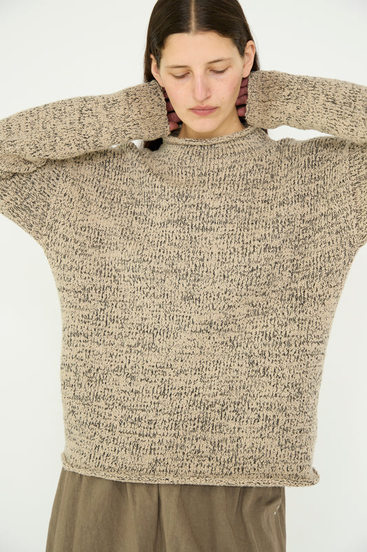 A model wearing the Marl Rollneck in Sisal by Lauren Manoogian and brown pants adjusts their hair against a light background.