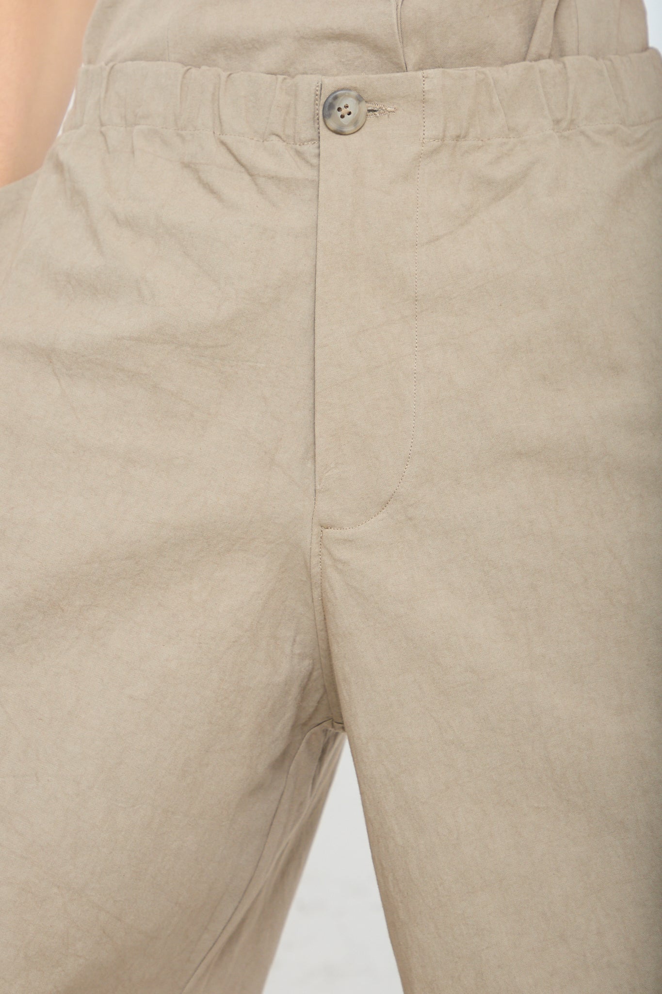 A close up of a woman wearing a pair of Lauren Manoogian's New Structure Pant in Drab (Olive brown). Up close view of waist band and button closure.