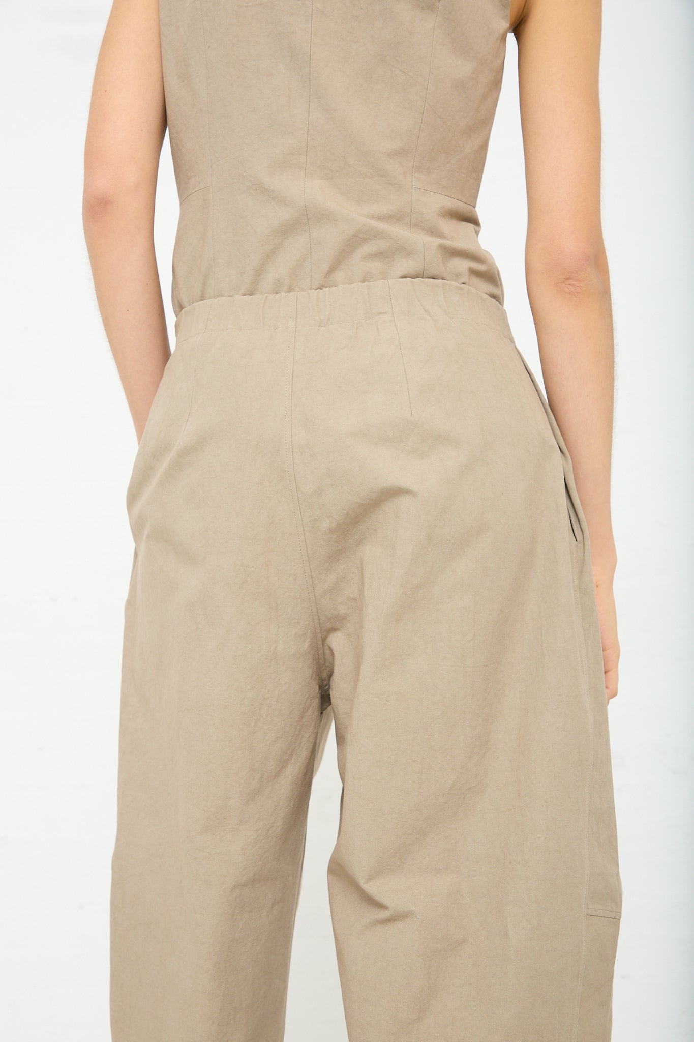 The back view of a woman wearing the Lauren Manoogian New Structure Pant in Drab, a relaxed fit, cotton jumpsuit with an elasticated waist. The model is wearing a matching top. Up close view.