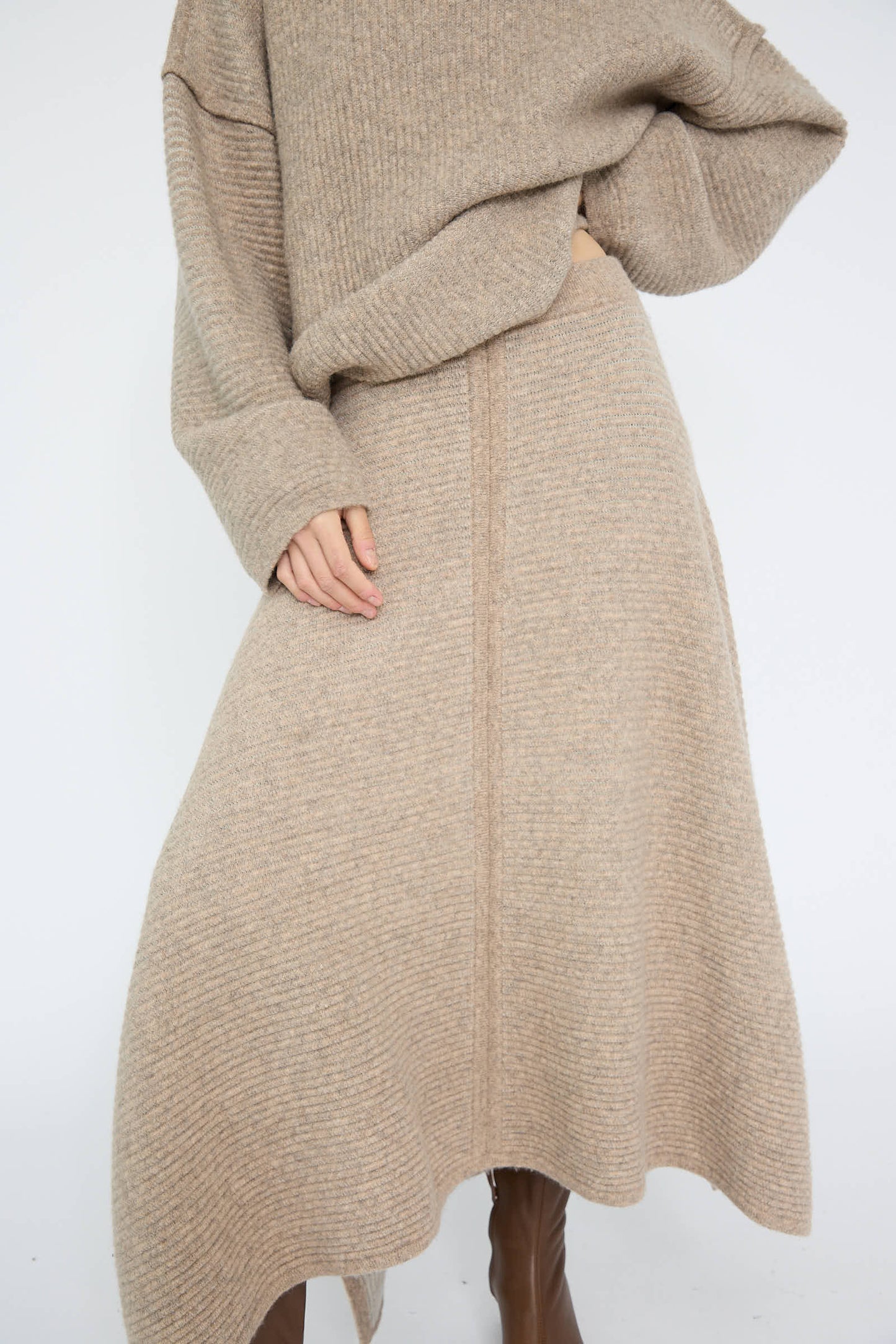 A person wearing a cozy draped silhouette with the Ottoman Panel Skirt in Moth/Carrara by Lauren Manoogian, paired with a beige knit sweater and brown boots.