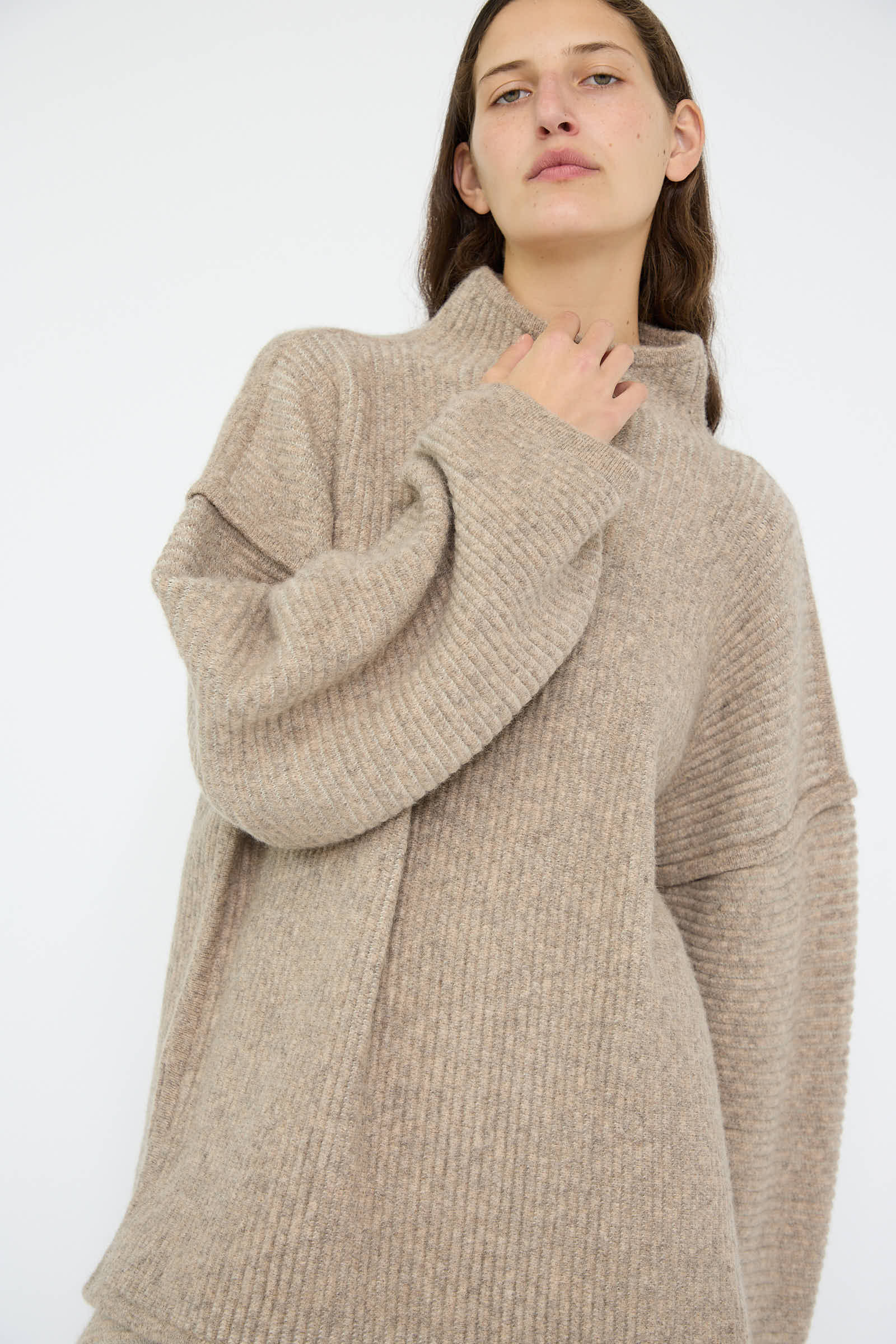 A person wearing the Ottoman Turtleneck in Moth / Carrara by Lauren Manoogian, an oversized and ribbed sweater crafted from a luxurious wool alpaca blend, stands against a plain white background.