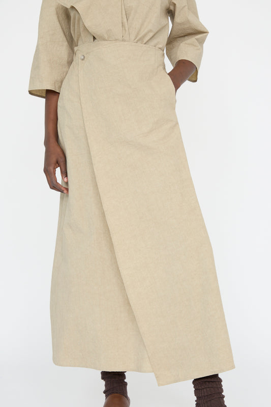 Against a plain background, a person is elegantly dressed in Lauren Manoogian's Panel Skirt in Drab, a cotton blend wrap-around maxi skirt paired with a matching long-sleeved top.