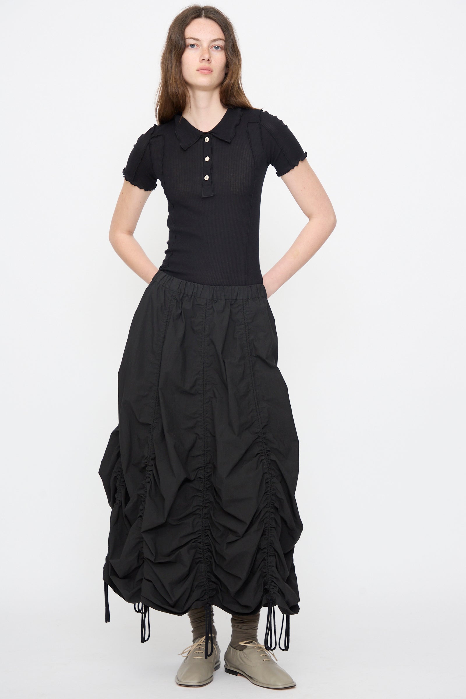 Woman in black short-sleeve collared shirt paired with the Parachute Skirt in Black by Lauren Manoogian, a midi skirt featuring subtle ruching.