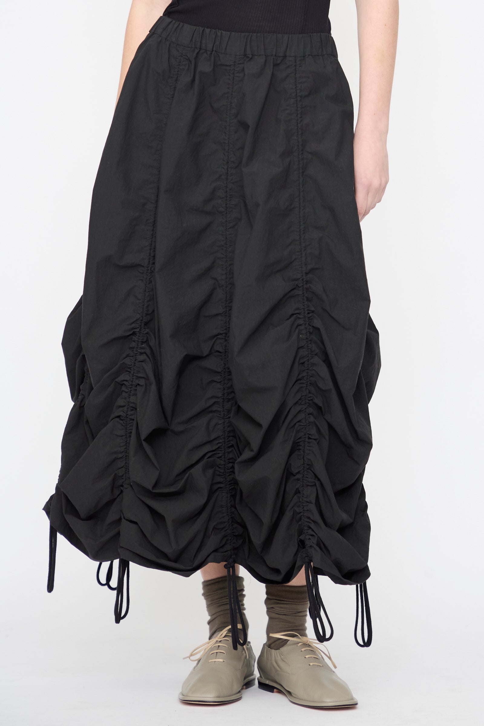 A person wears the Lauren Manoogian Parachute Skirt in Black, styled with olive socks and tan shoes.
