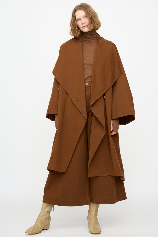 Person wearing the Lauren Manoogian Planes Coat in Rust—an oversized brown cotton coat—paired with a brown turtleneck top, wide-leg brown pants, and beige heeled boots, standing against a plain white background.