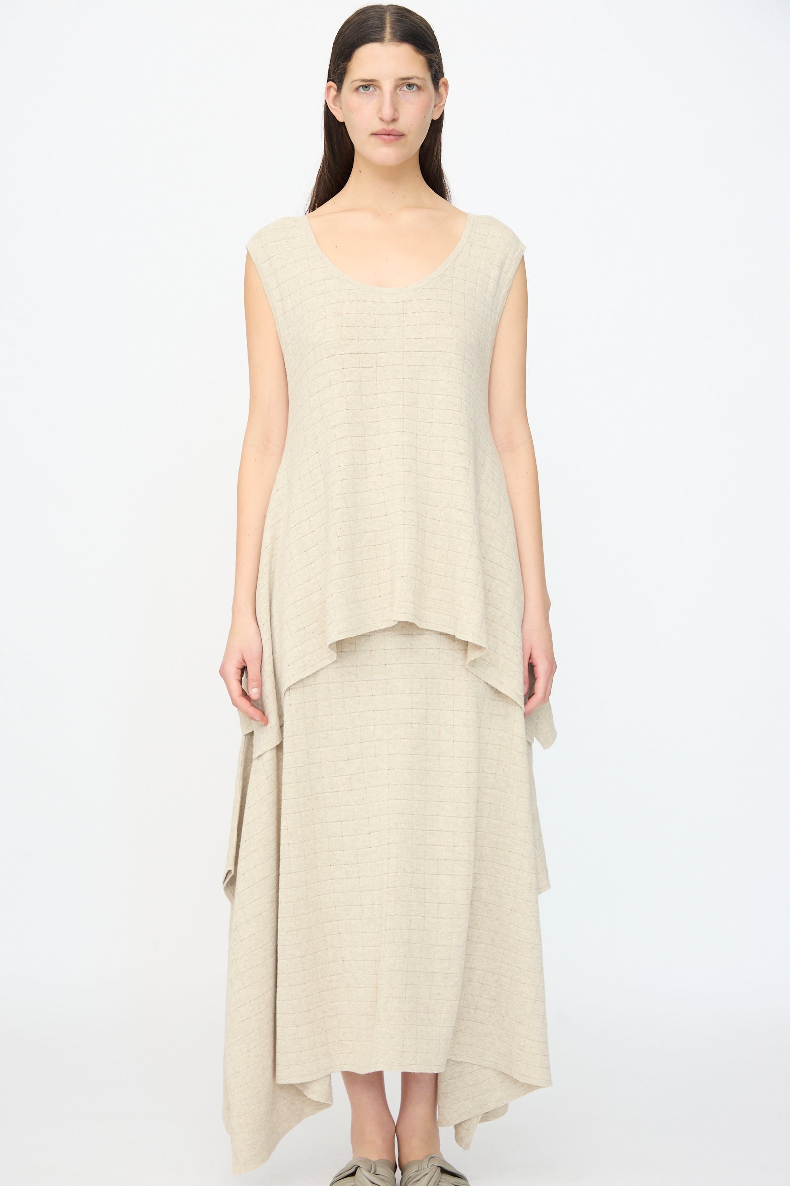 A woman stands facing forward against a white background, wearing the Lauren Manoogian Planes Tank in Flax—a relaxed fit, sleeveless, beige layered maxi dress with an uneven hem.