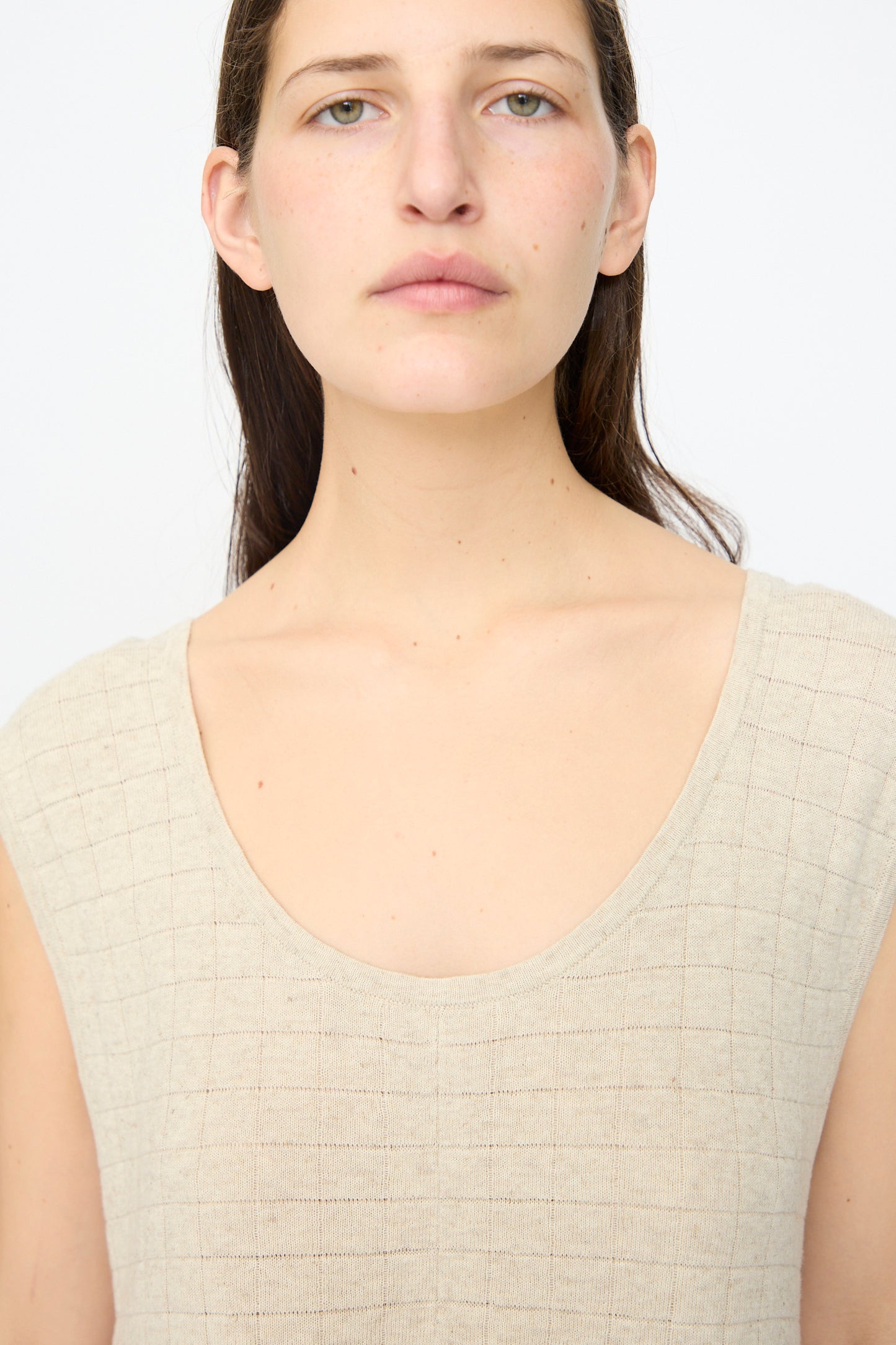 A person with long brown hair wears the Lauren Manoogian Planes Tank in Flax, a beige, sleeveless, textured linen top, and looks directly at the camera against a plain white background.
