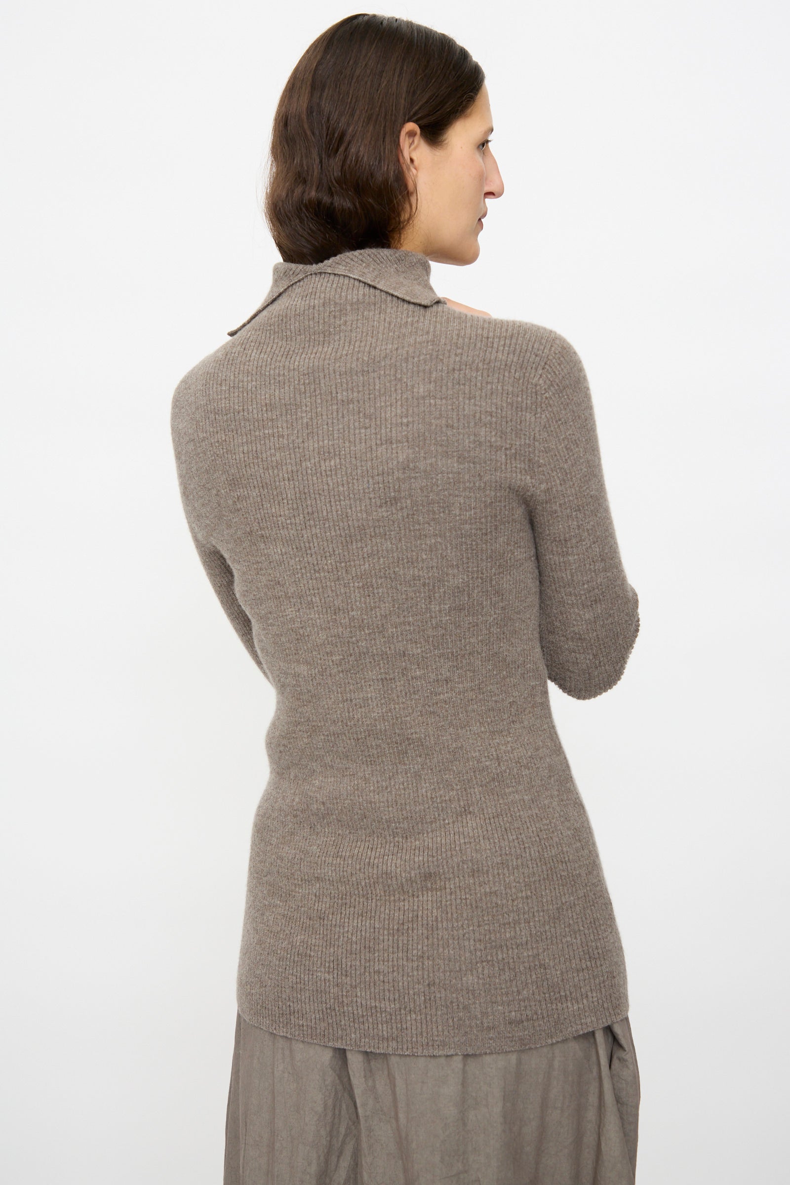A person with medium-length brown hair is shown from the back wearing Lauren Manoogian's Rib Split Turtleneck in Cinder and a gray skirt, standing against a plain white background.