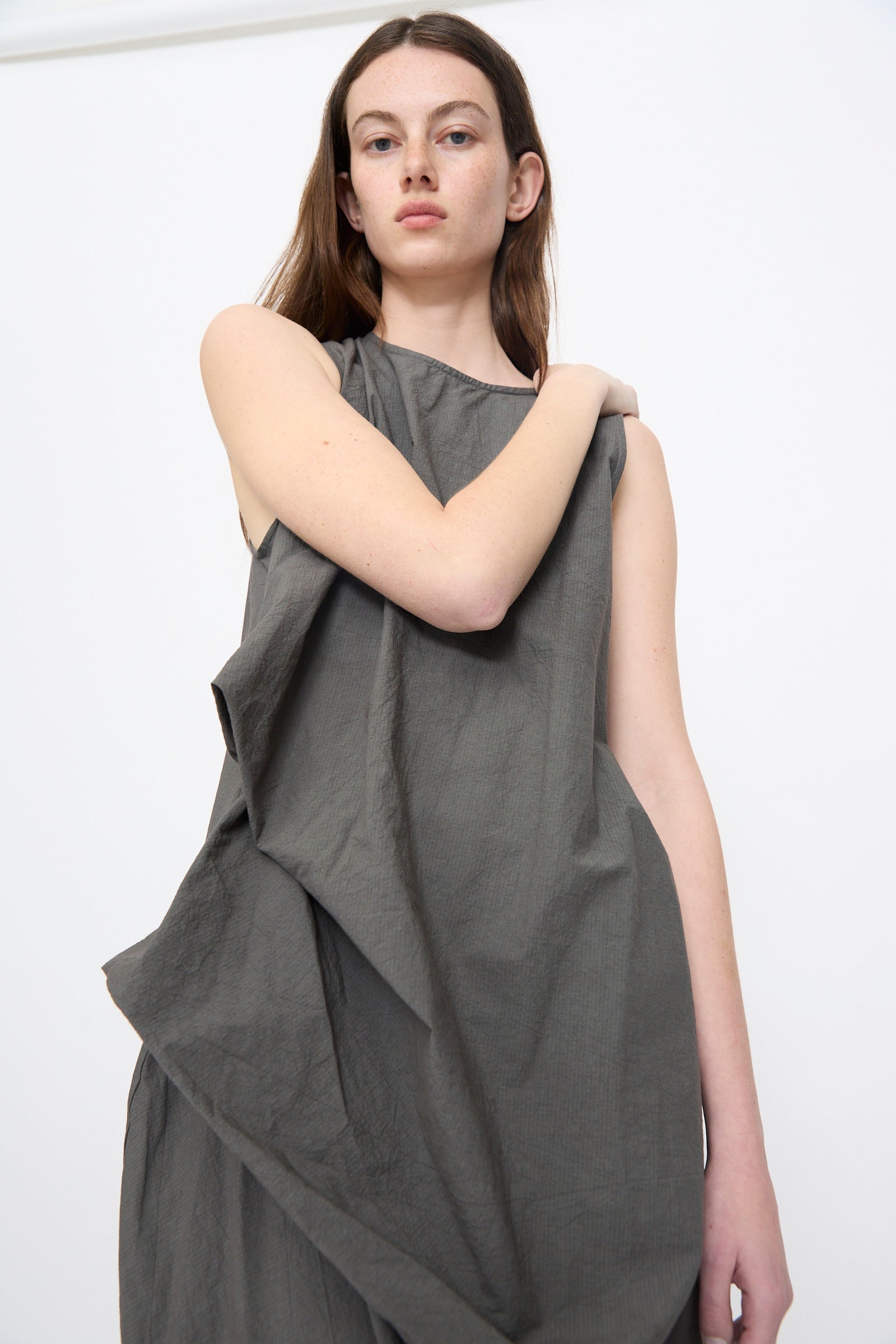A person with long brown hair wears the Lauren Manoogian Ripstop Dress in Coal, a sleeveless midi style, standing against a plain white background and looking directly at the camera.