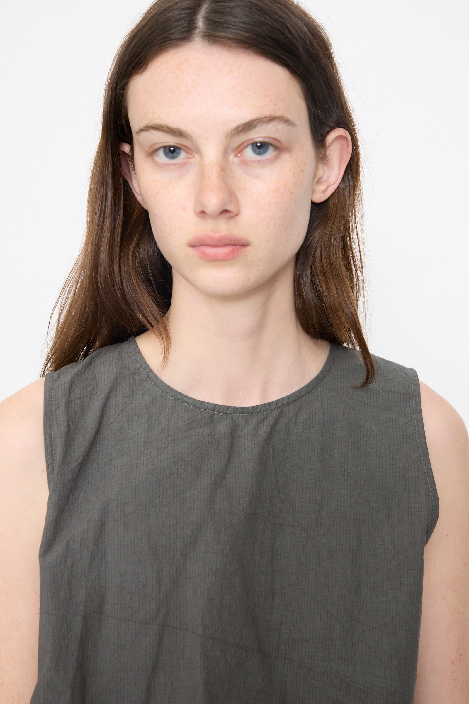 A model wears the Lauren Manoogian Ripstop Dress in Coal, a sleeveless crew-neck piece with an asymmetrical gathered silhouette and textured fabric, photographed from the chest up against a white background.