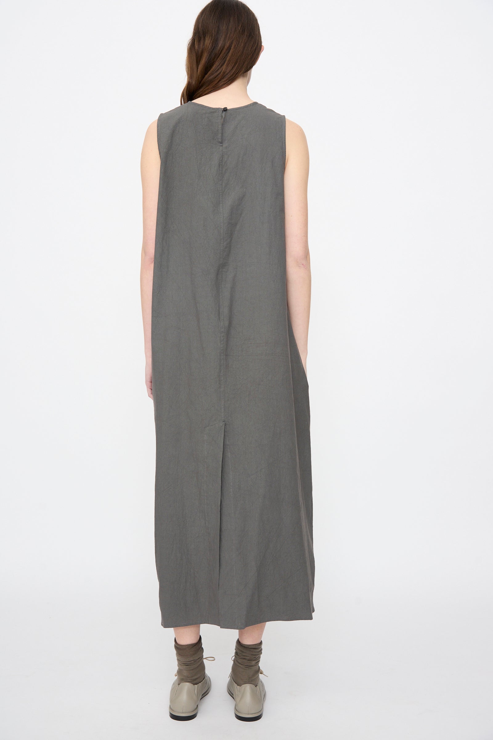 Back view of a person wearing the Lauren Manoogian Ripstop Dress in Coal, a sleeveless midi dress with a back slit, styled with tan ballet flats and khaki socks.