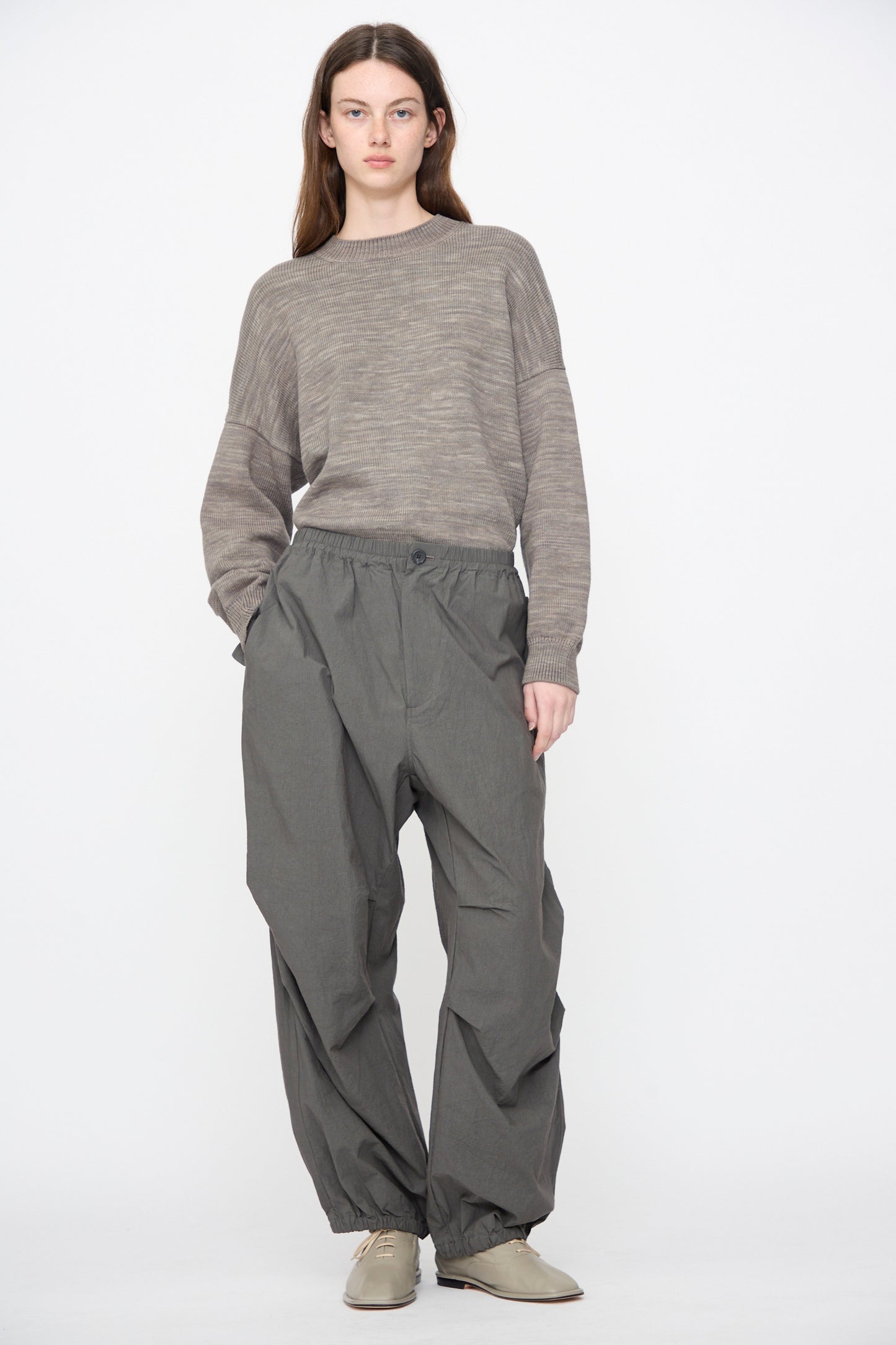 A model wears Lauren Manoogian Ripstop Pants in Coal, a taupe ribbed knit sweater, and light grey lace-up shoes against a white background.