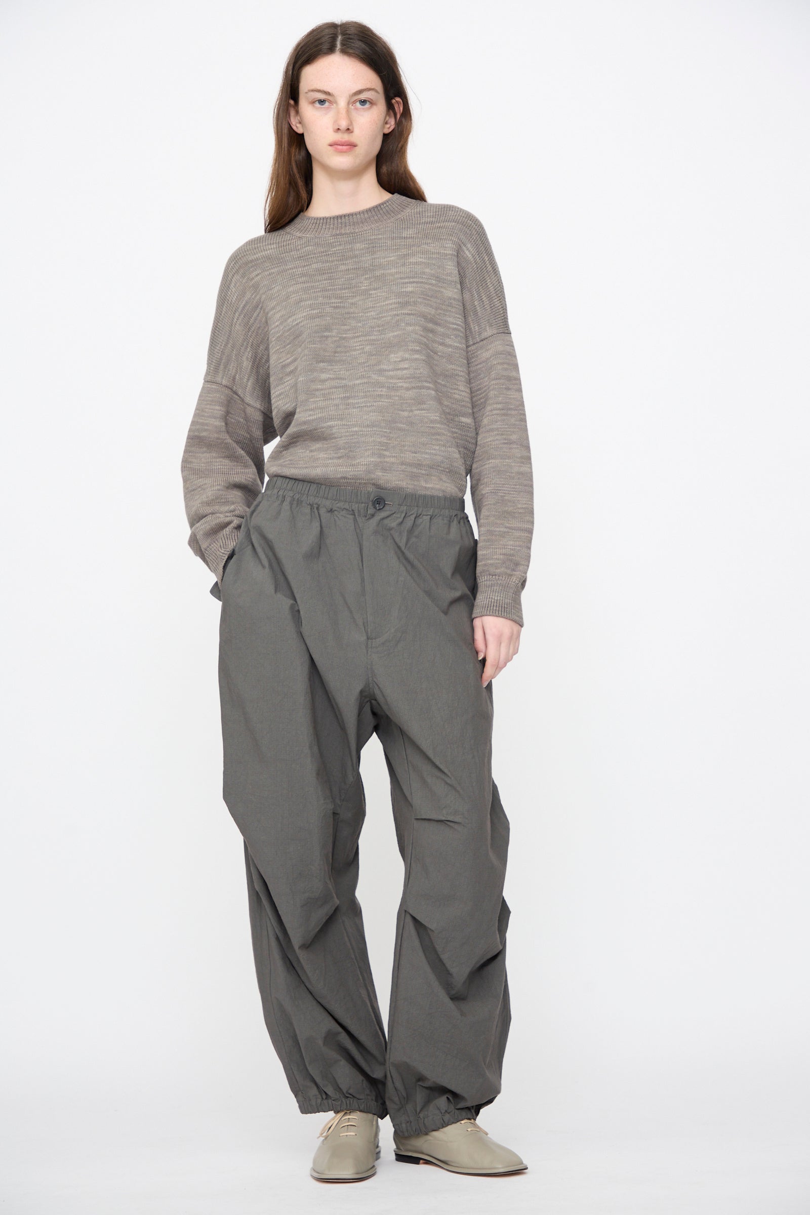 A model wears Lauren Manoogian Ripstop Pants in Coal, a taupe ribbed knit sweater, and light grey lace-up shoes against a white background.
