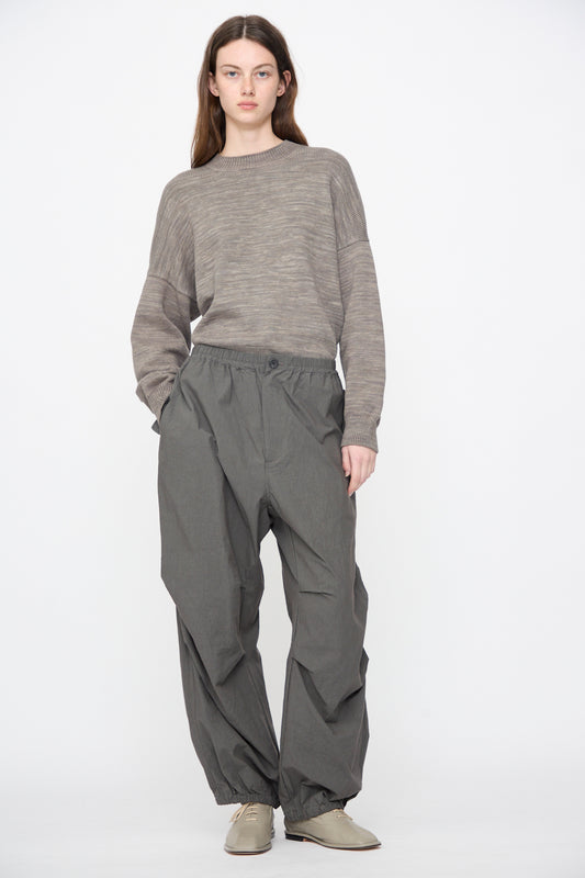 A model wears Lauren Manoogian Ripstop Pants in Coal, a taupe ribbed knit sweater, and light grey lace-up shoes against a white background.