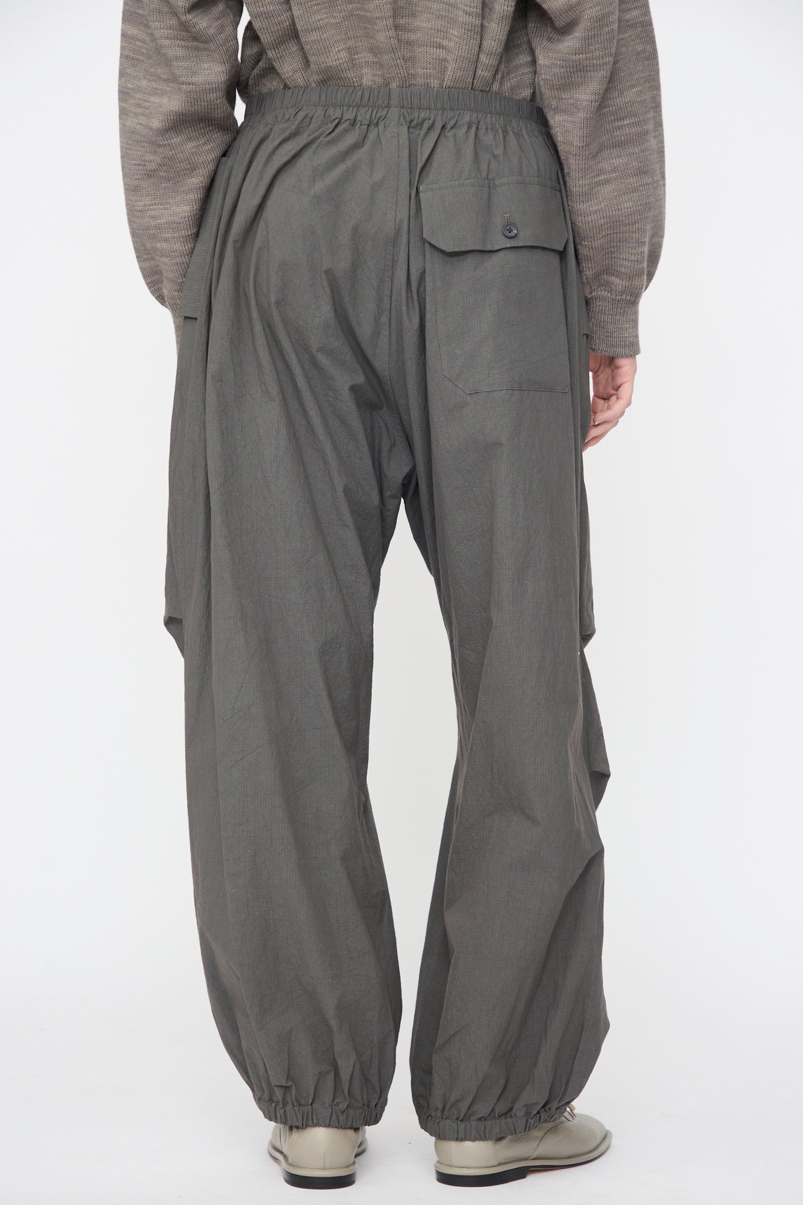 A person is seen from the back wearing Lauren Manoogian Ripstop Pants in Coal with an elastic waistband and ankles, paired with a gray textured top and light-colored shoes.