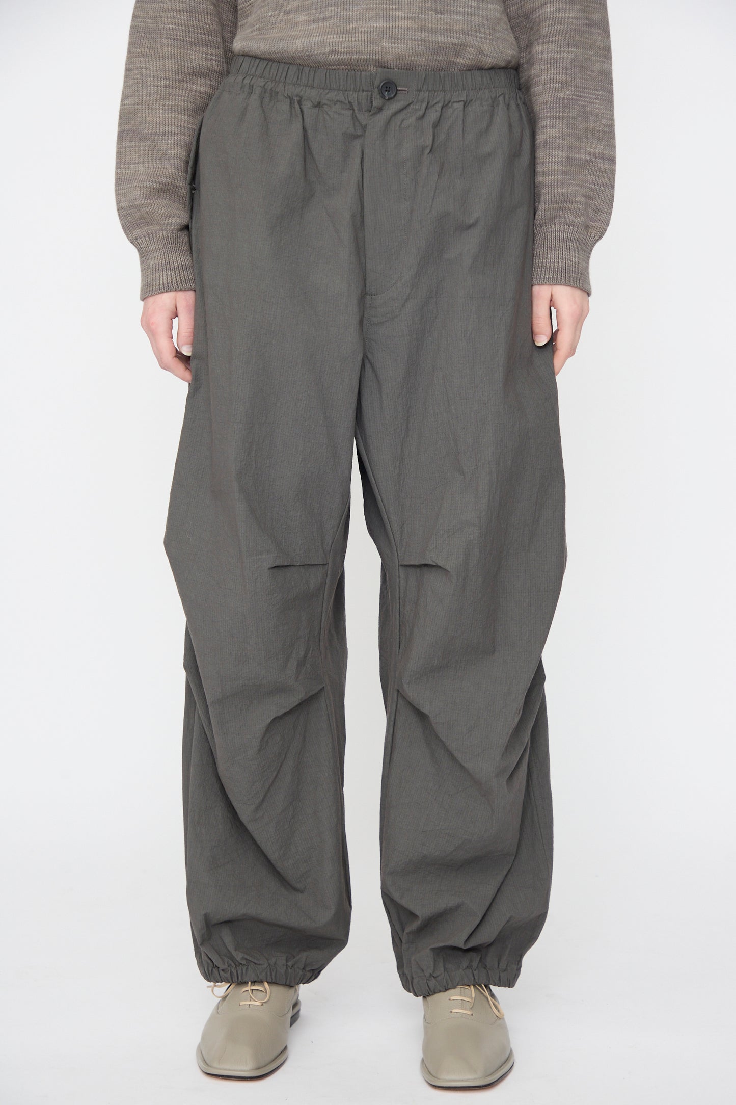 Full-length shot of a person wearing a brown knit sweater and Lauren Manoogian Ripstop Pants in Coal, paired with taupe lace-up shoes.