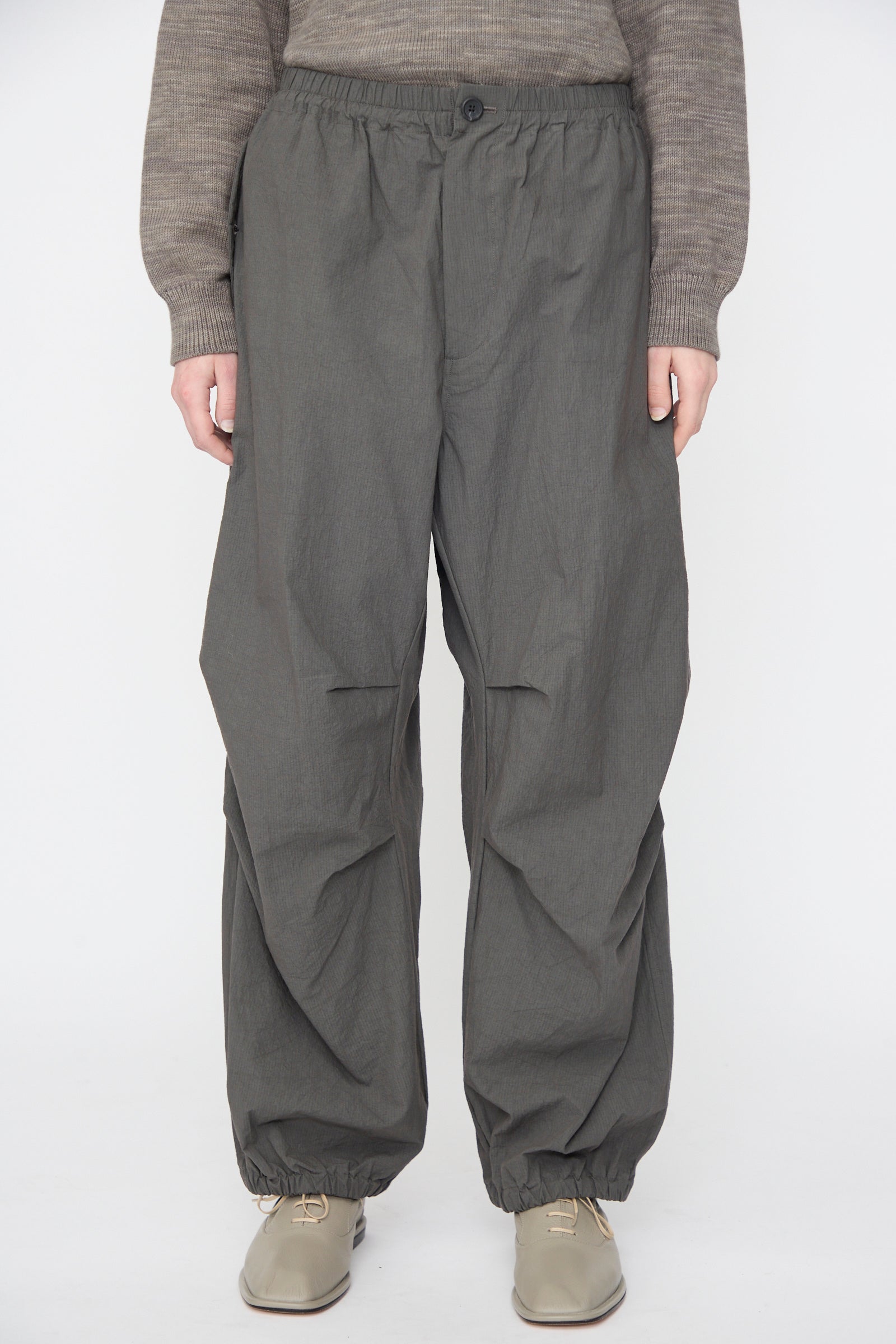 Full-length shot of a person wearing a brown knit sweater and Lauren Manoogian Ripstop Pants in Coal, paired with taupe lace-up shoes.