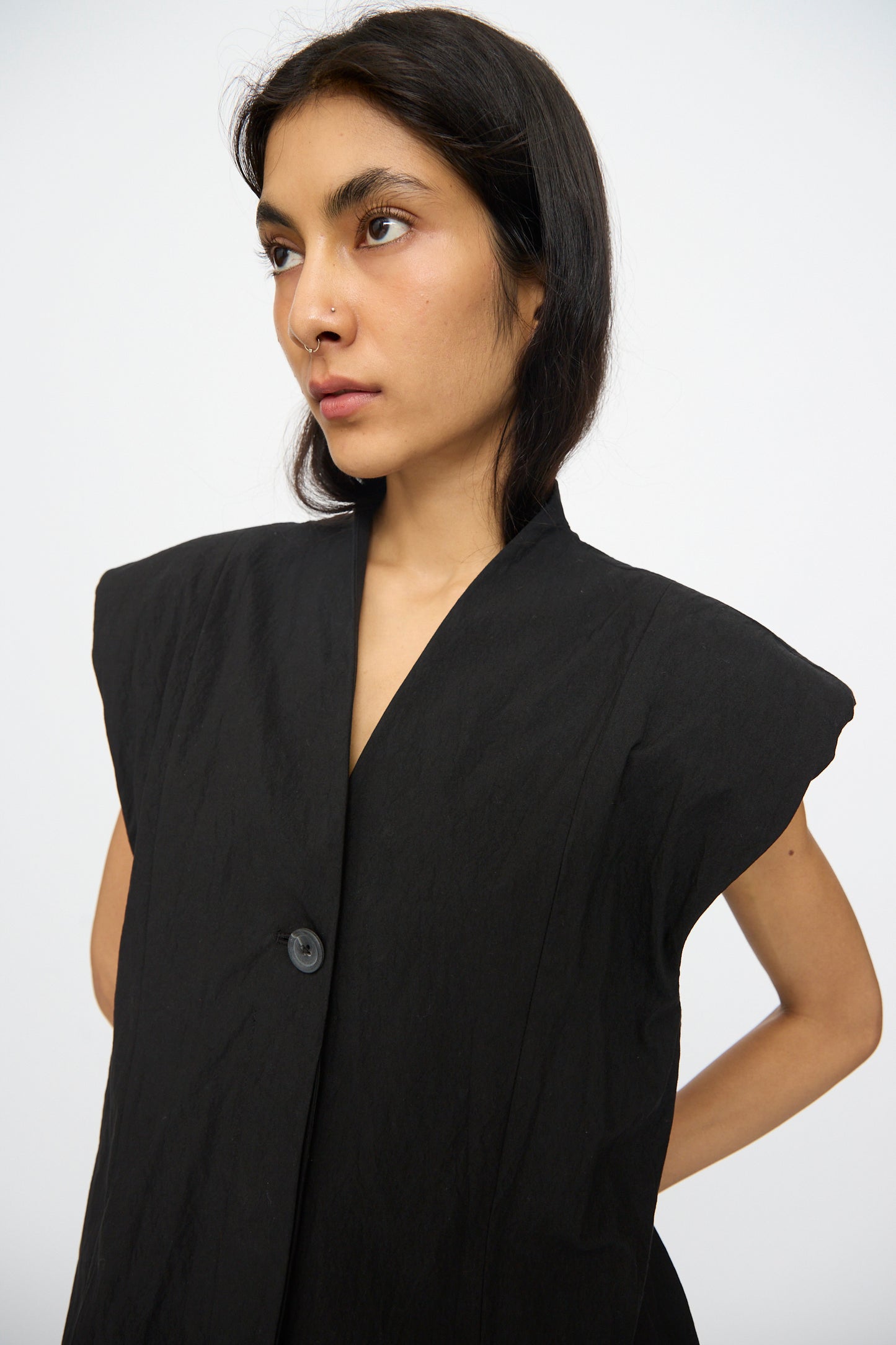 A woman with long dark hair models the Lauren Manoogian Shoulder Gilet in Black—a cotton-blend vest with broad shoulders—against a plain white background.
