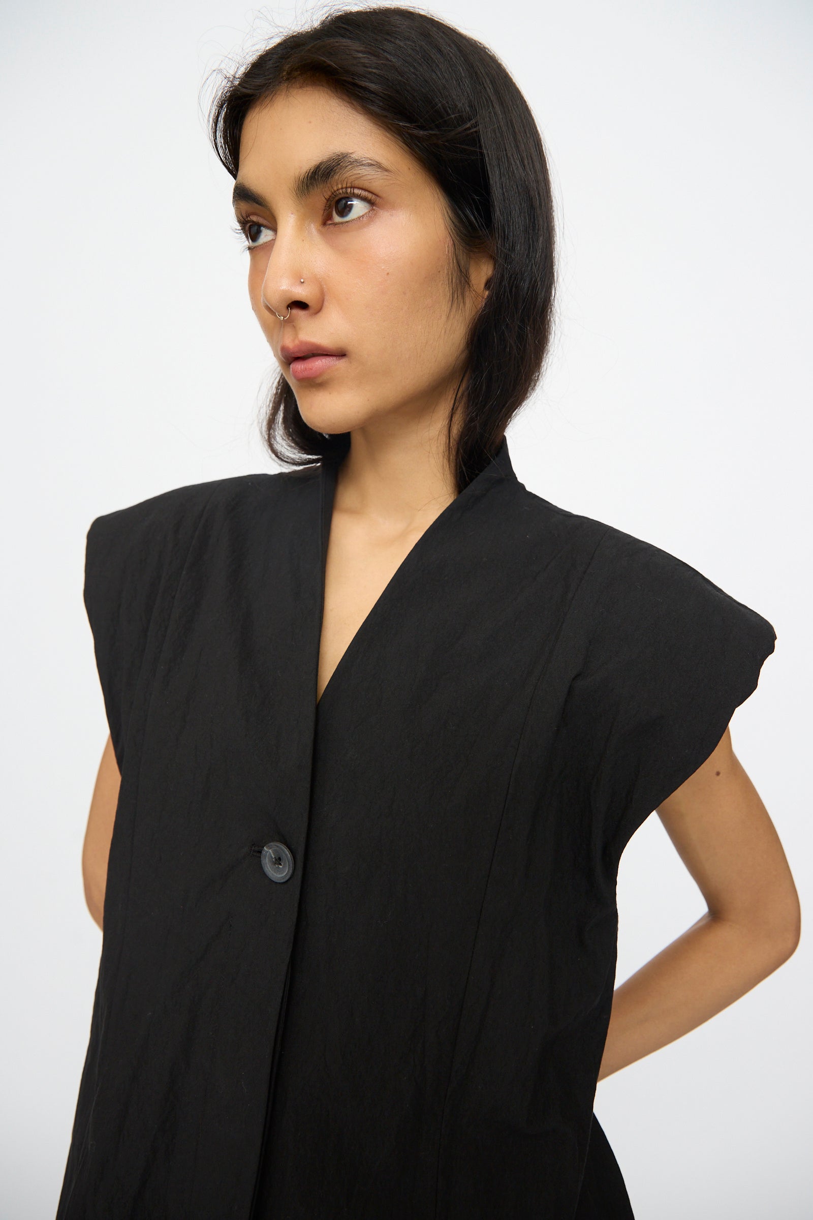 A woman with long dark hair models the Lauren Manoogian Shoulder Gilet in Black—a cotton-blend vest with broad shoulders—against a plain white background.
