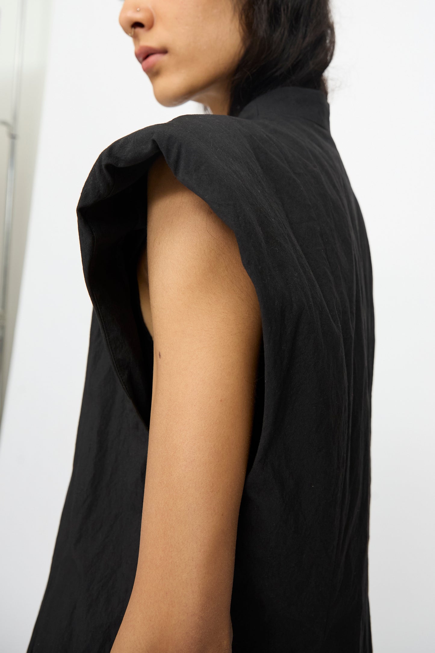 A person is shown in profile against a plain background, wearing the Lauren Manoogian Shoulder Gilet in Black, highlighting the modern style of this cotton blend piece.