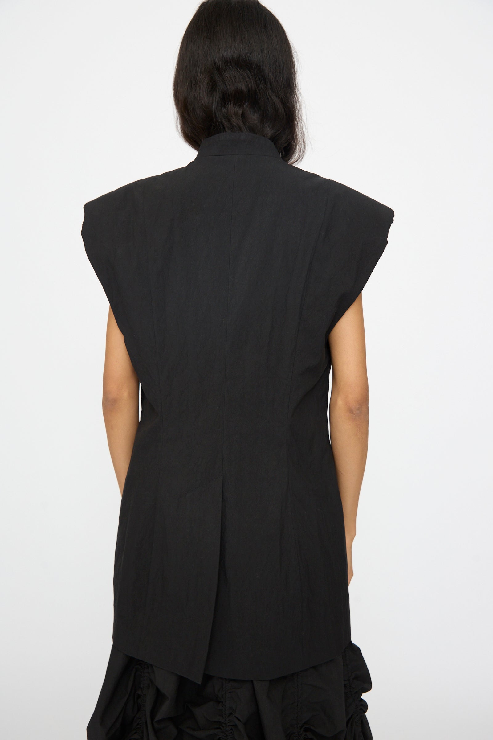 A person is shown from the back wearing the Lauren Manoogian Shoulder Gilet in Black with a matching skirt, standing against a plain white background.