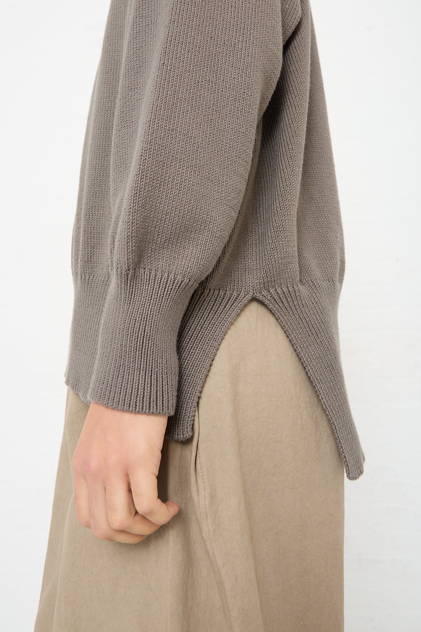 The side view of a woman wearing a Simple Crewneck in Rock (Olive Brown) by Lauren Manoogian and beige colored pants.