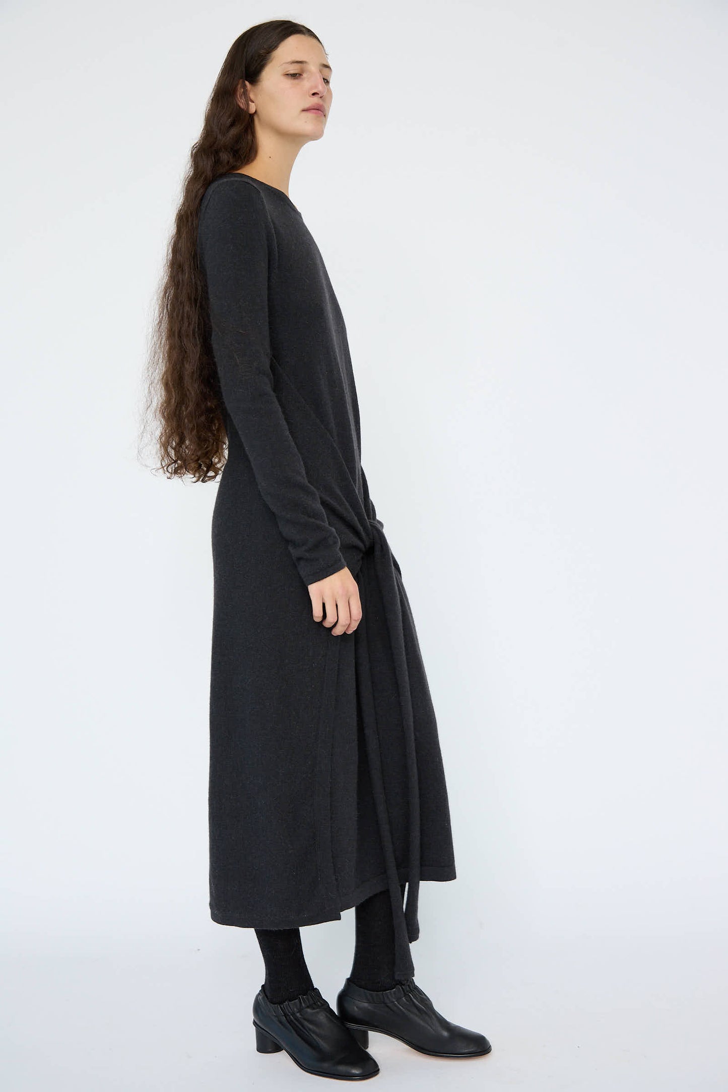 A person with long hair stands against a white background, wearing the Lauren Manoogian Sleeves Dress in Ink, a relaxed fit maxi dress, and black shoes.