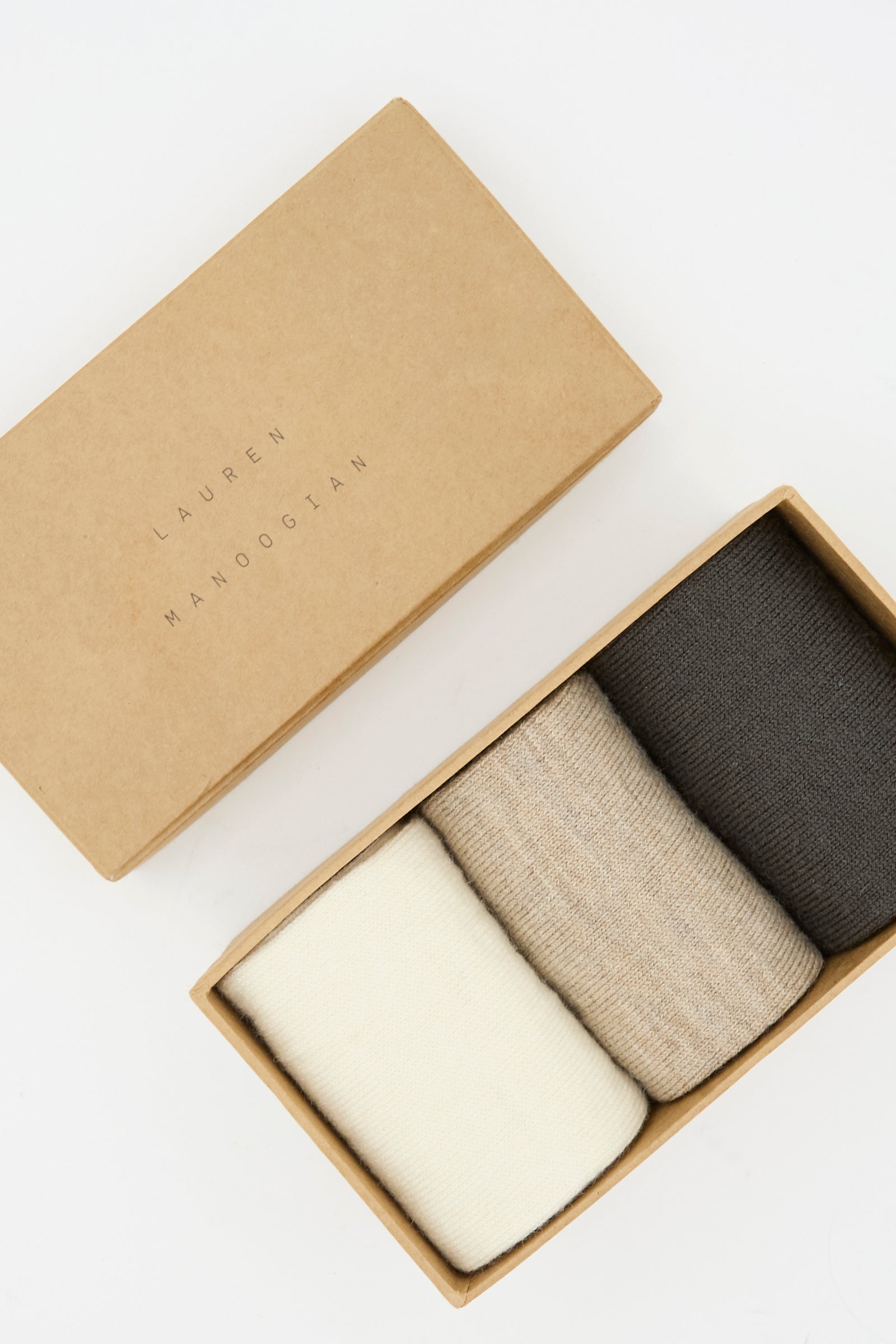 A Lauren Manoogian Sock Set in Mix contains three rolled pairs of alpaca wool socks—in cream, beige, and dark gray—made in Peru.