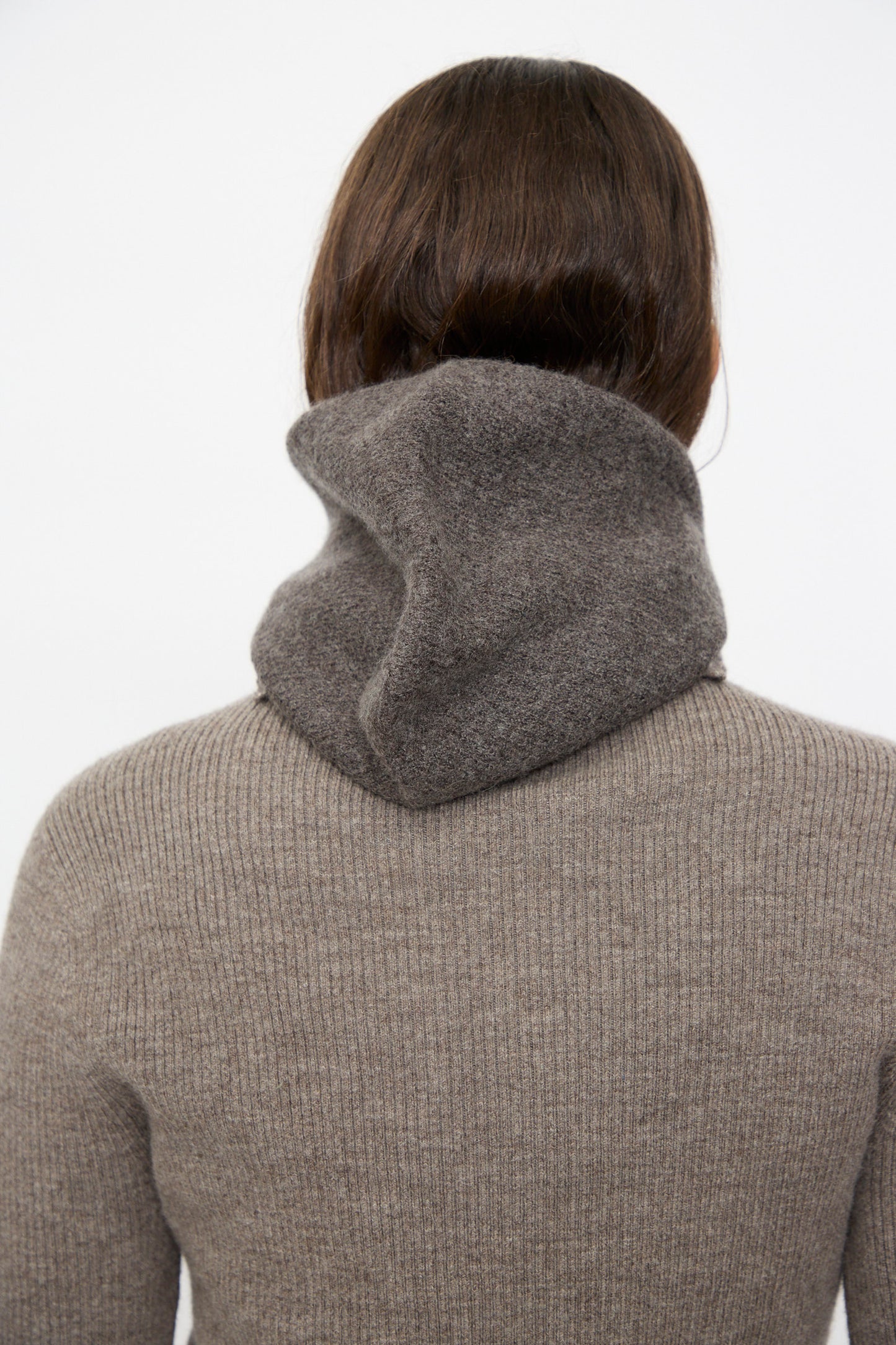 A person with brown hair is shown from behind, wearing a ribbed taupe sweater with a high, folded collar and the Lauren Manoogian Soft Balaclava in Blackened.