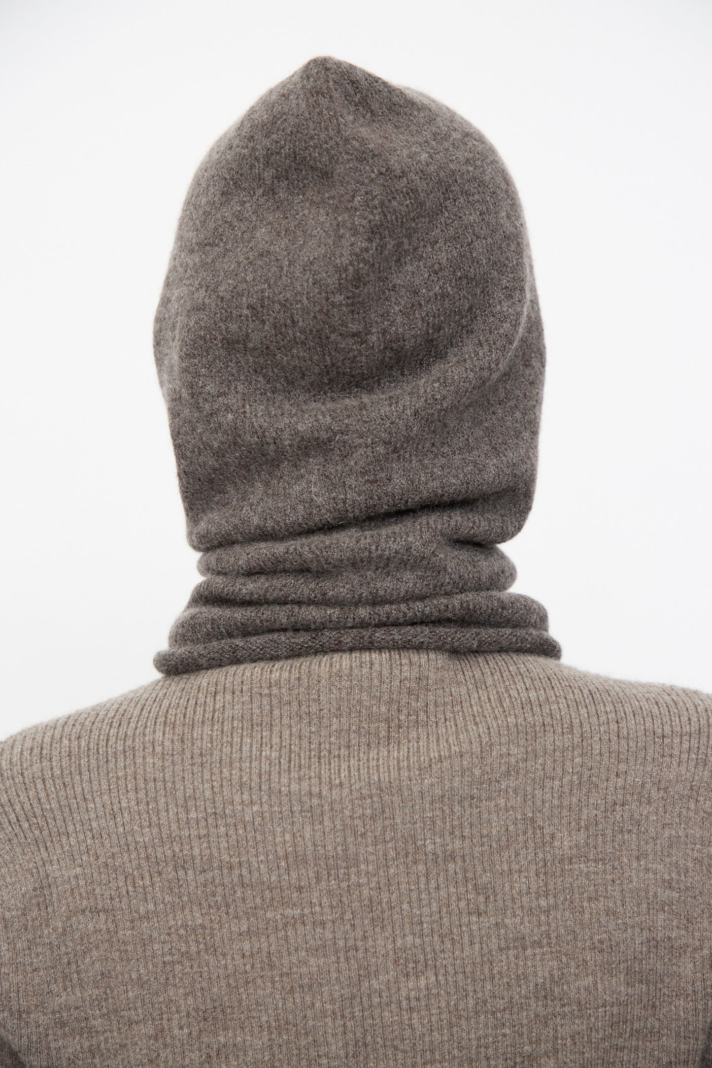 A person shown from the back against a plain white background wears a ribbed brown hooded sweater paired with the Lauren Manoogian Soft Balaclava in Blackened.