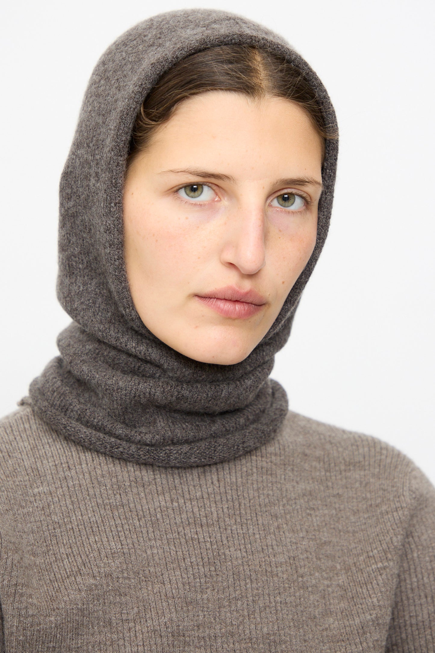 A person with light skin and green eyes wears the Lauren Manoogian Soft Balaclava in Blackened, facing forward against a plain white background.
