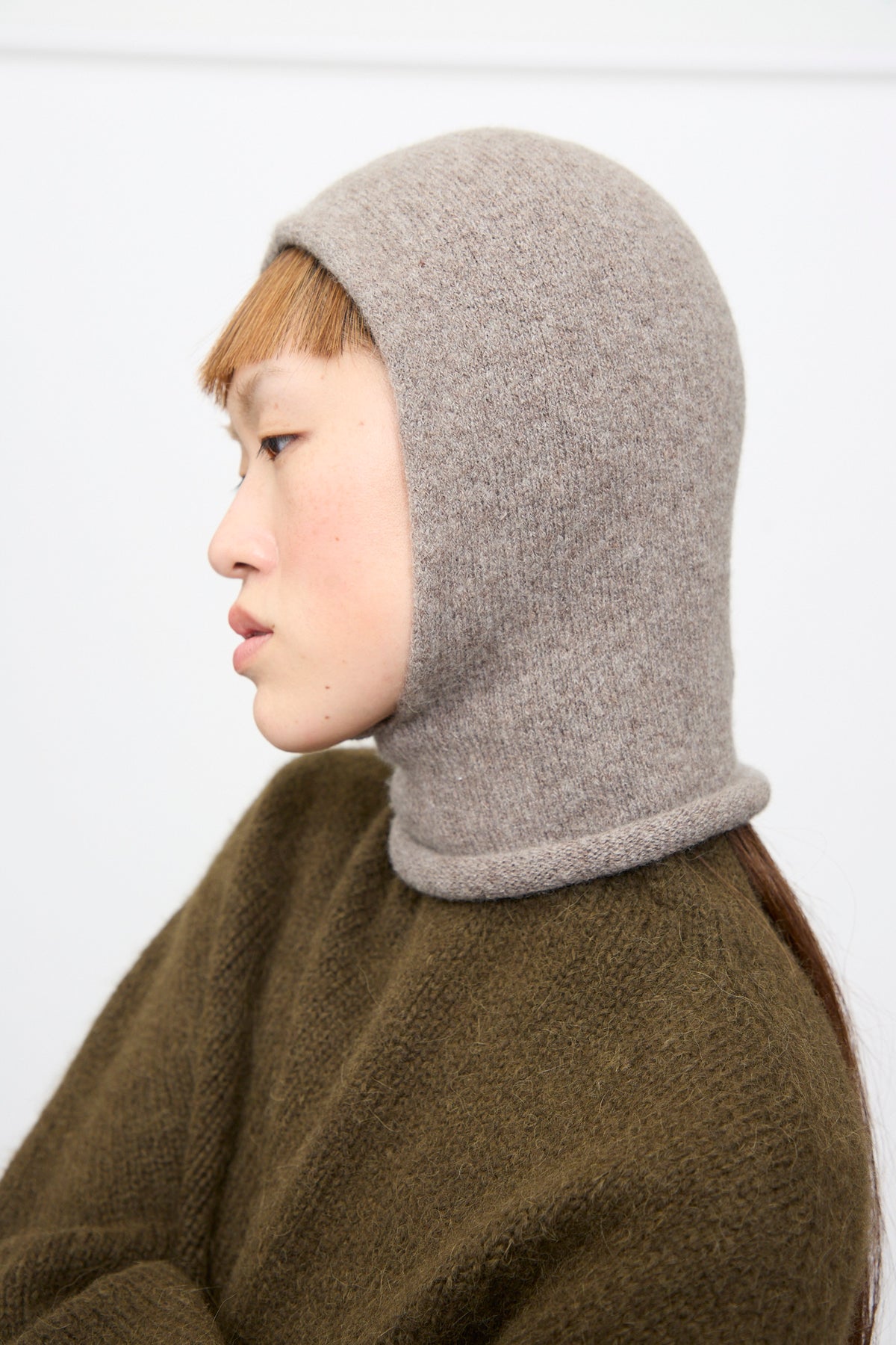 A person in profile wearing a fitted, light grey handloomed Lauren Manoogian Soft Balaclava in Grey Melange.
