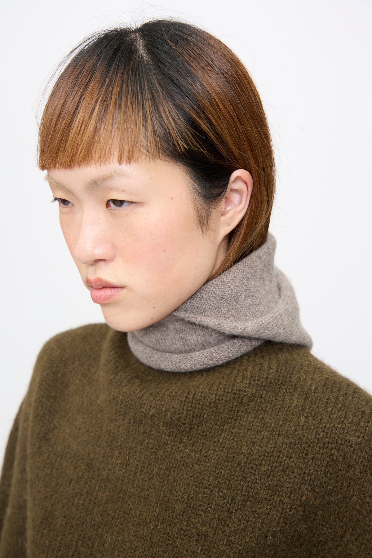 A person wearing a handloomed Lauren Manoogian Soft Balaclava in Grey Melange tucked into an olive green sweater.