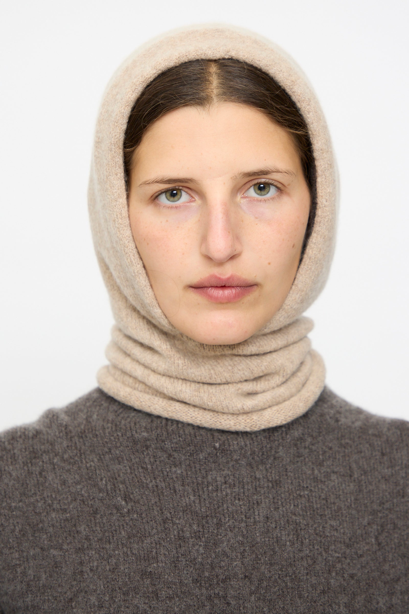 A person with light skin and straight brown hair wears the Lauren Manoogian Soft Balaclava in Oak and a dark brown sweater, looking at the camera against a plain background. Crafted in Peru.