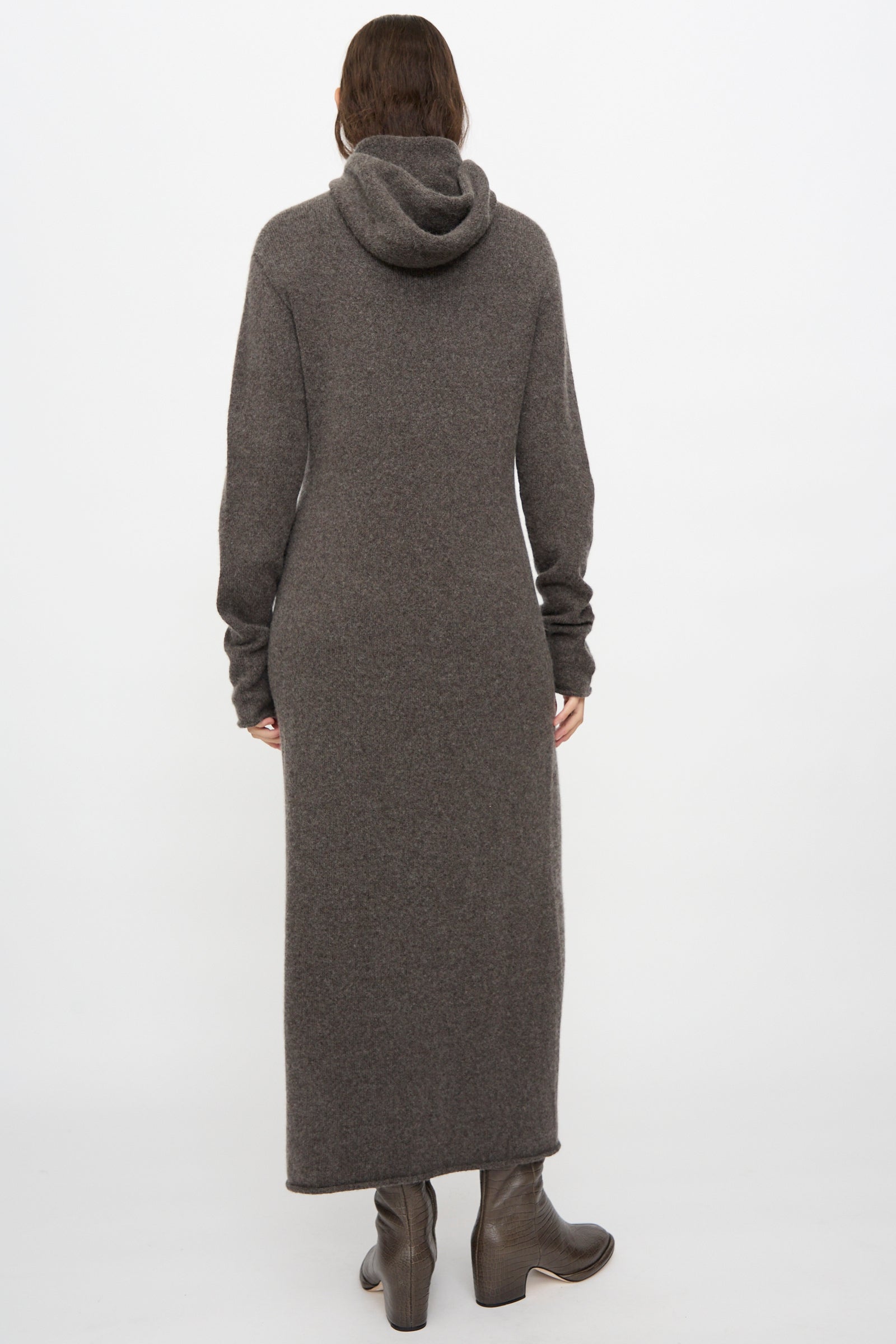 A person stands with their back to the camera against a plain white background, wearing the Lauren Manoogian Soft Balaclava Dress in Blackened and brown heeled boots.