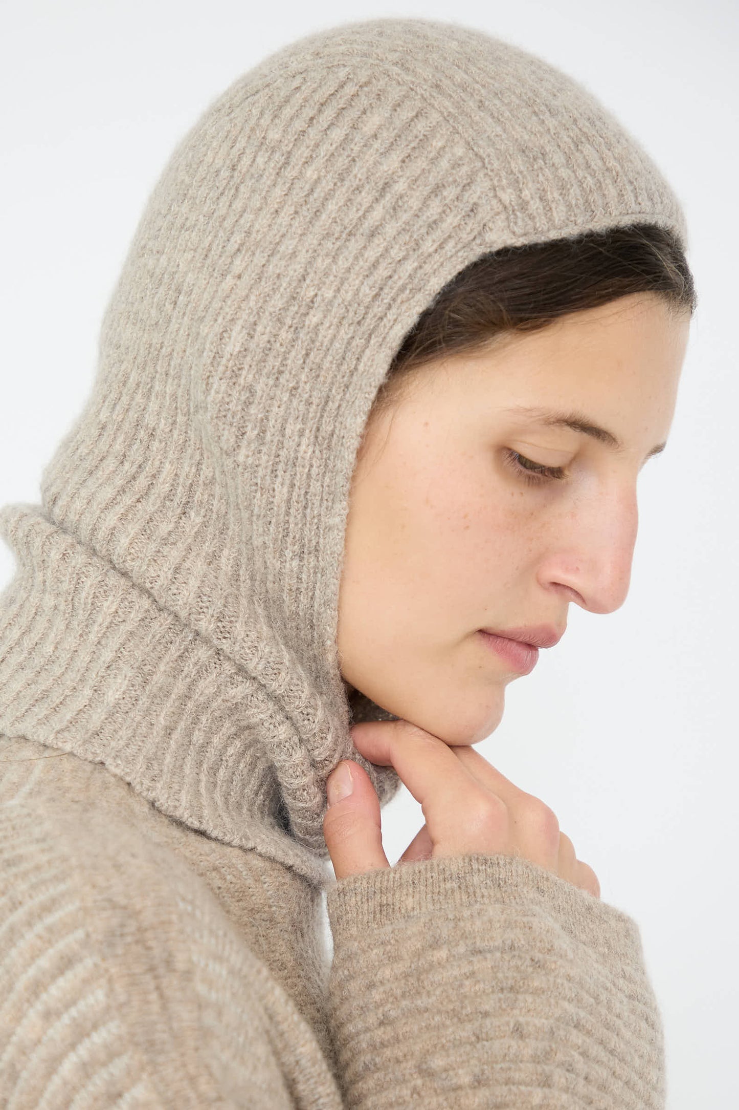 A person in the Soft Rib Balaclava in Dust by Lauren Manoogian, looking down, against a plain white background.