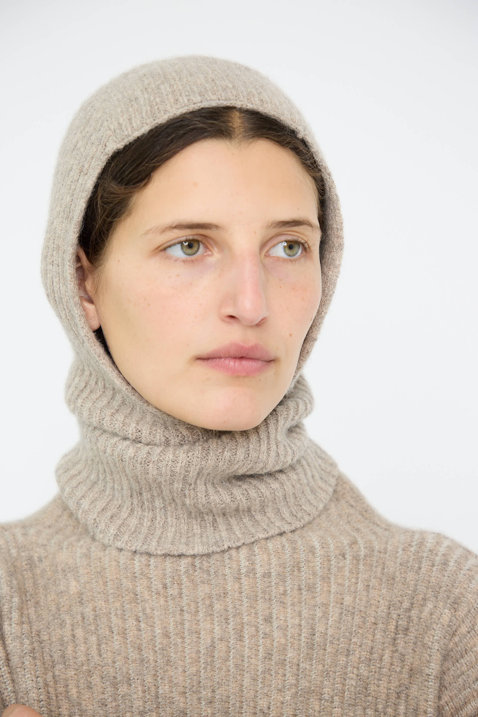 A person wearing a Lauren Manoogian Soft Rib Balaclava in Dust glances to the side against a plain background.