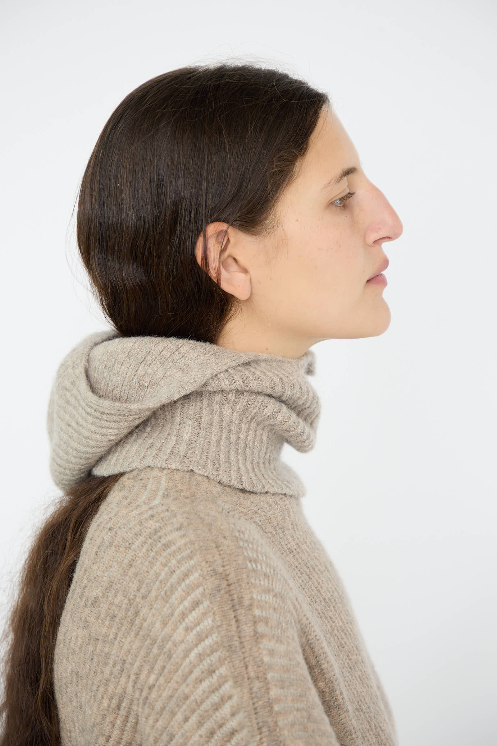 A person with long brown hair is seen in profile, wearing the Soft Rib Balaclava in Dust by Lauren Manoogian against a plain background.