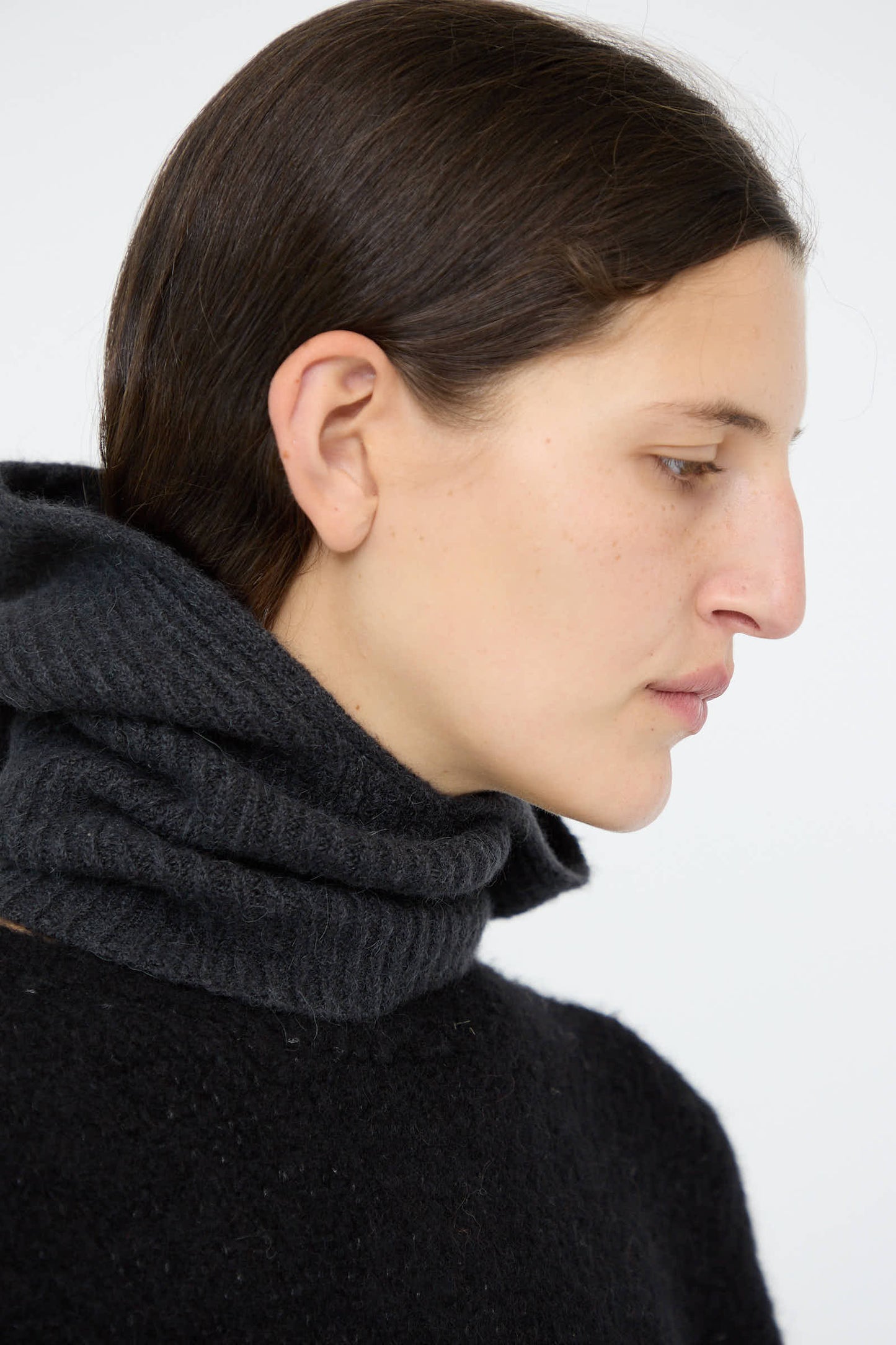 A person with long dark hair wearing a black cashmere sweater and an "Ink" Soft Rib Balaclava from Lauren Manoogian, looking to the side against a plain background.