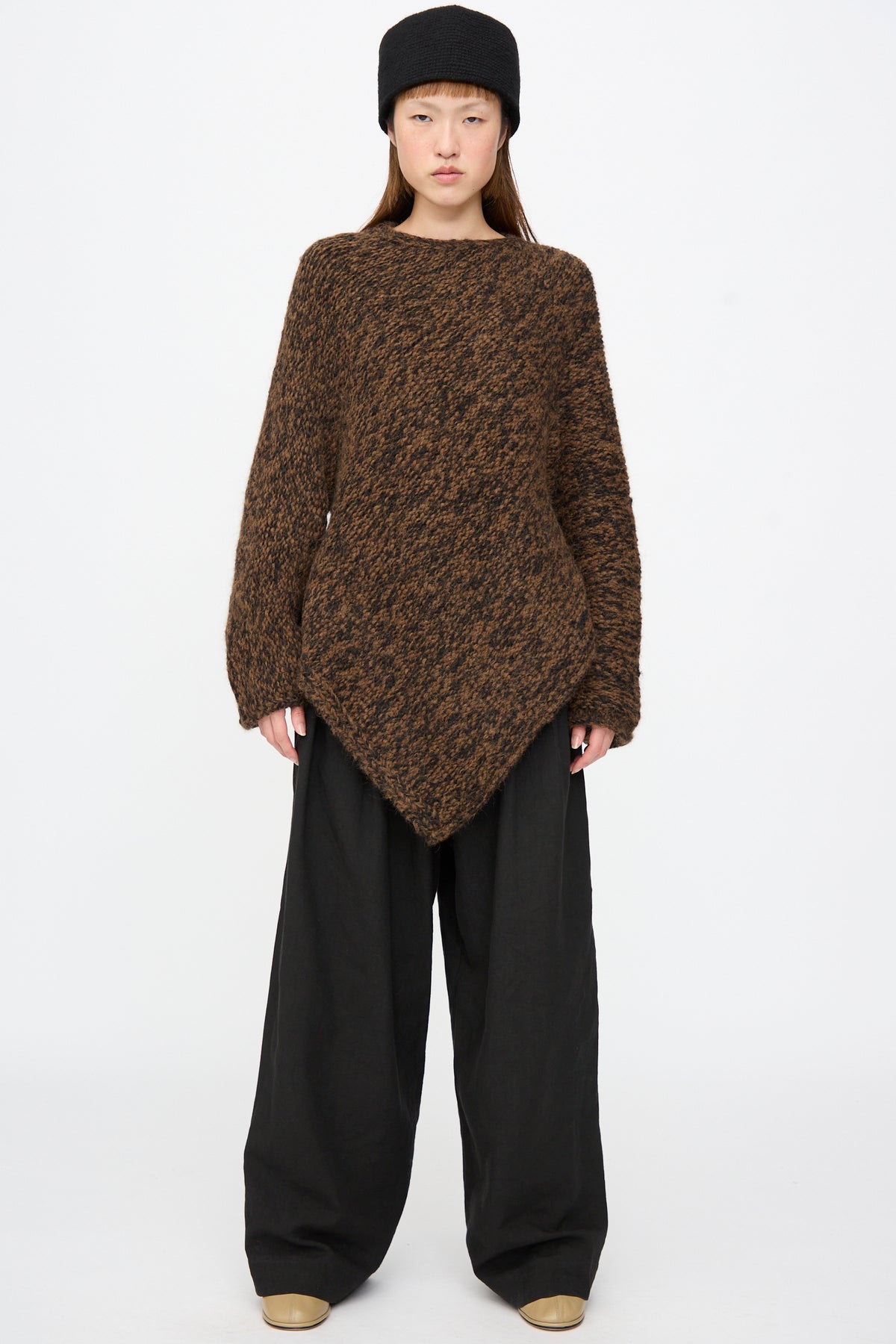 A person wears a brown, asymmetrical, textured knit sweater and Lauren Manoogian Soft Trouser in Black.