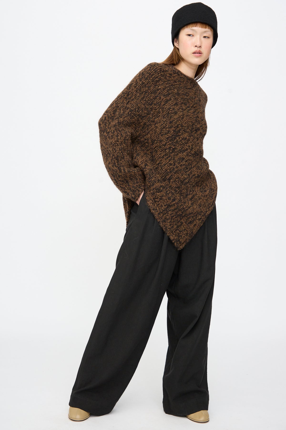 A person wearing a black hat, a brown textured sweater, and Lauren Manoogian Soft Trouser in Black.
