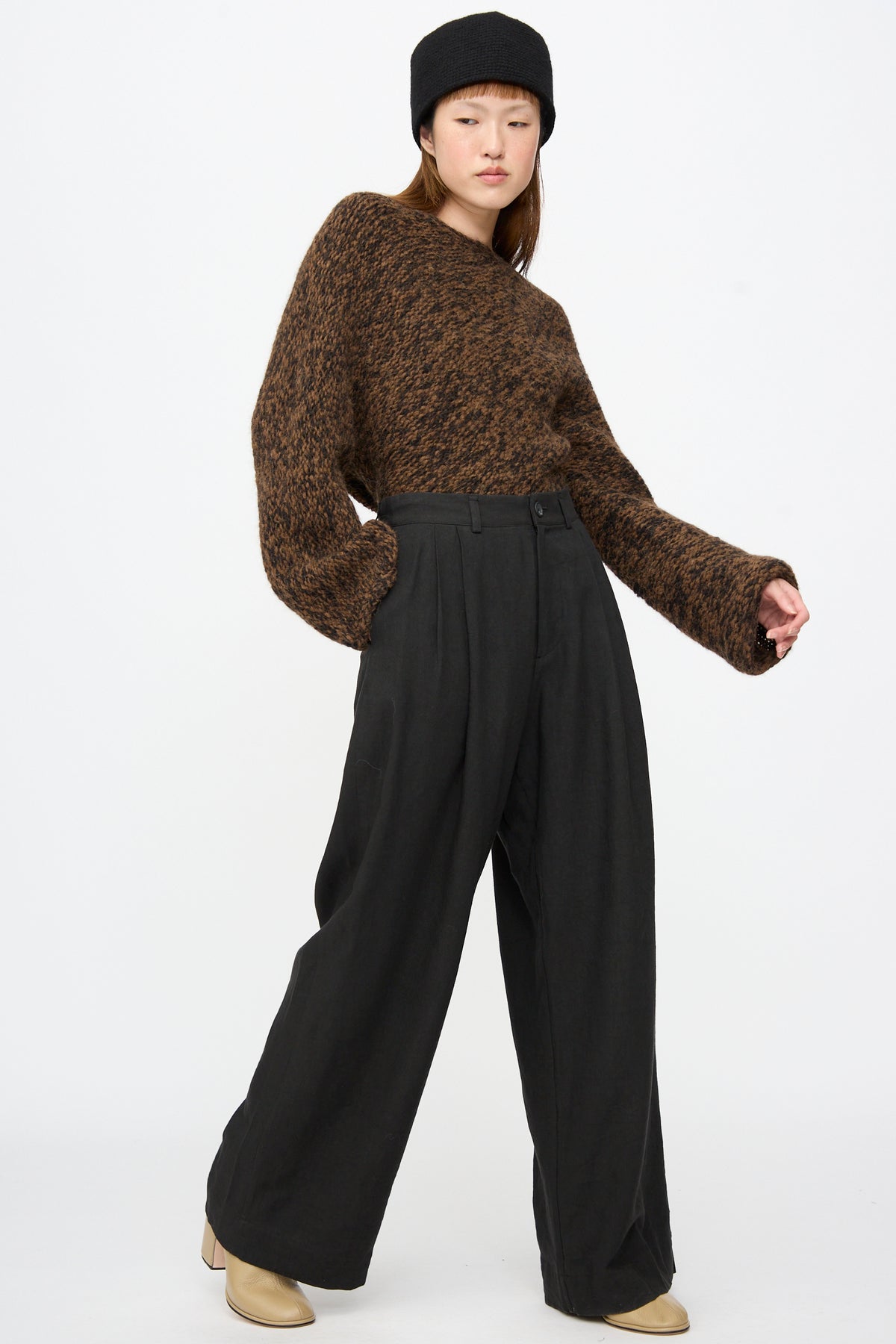 A person wearing a brown speckled sweater, a black hat, and black Lauren Manoogian Soft Trouser.