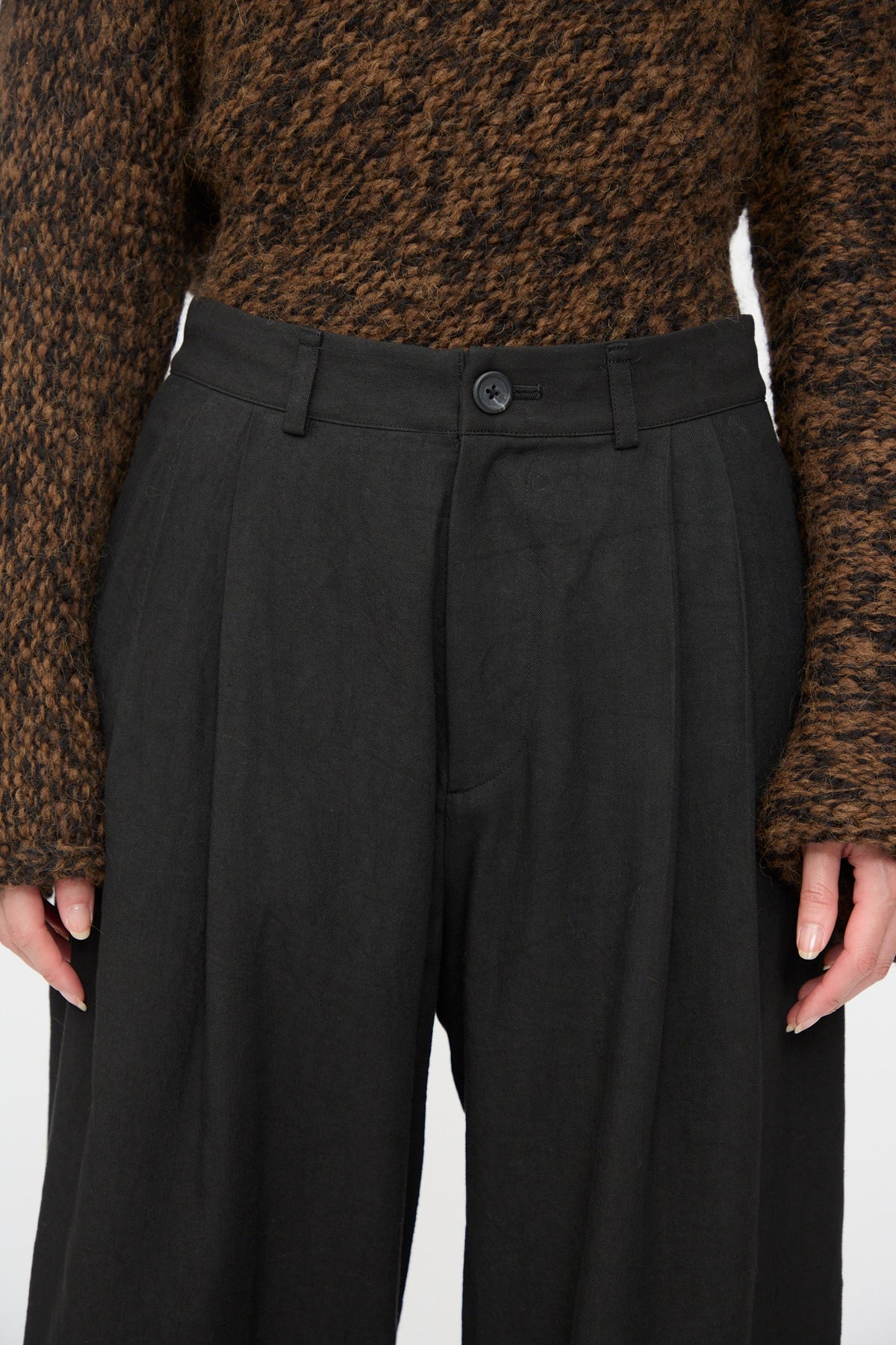 Lauren Manoogian Soft Trouser in Black featuring a high waist, button closure, and belt loops, worn with a brown patterned sweater.