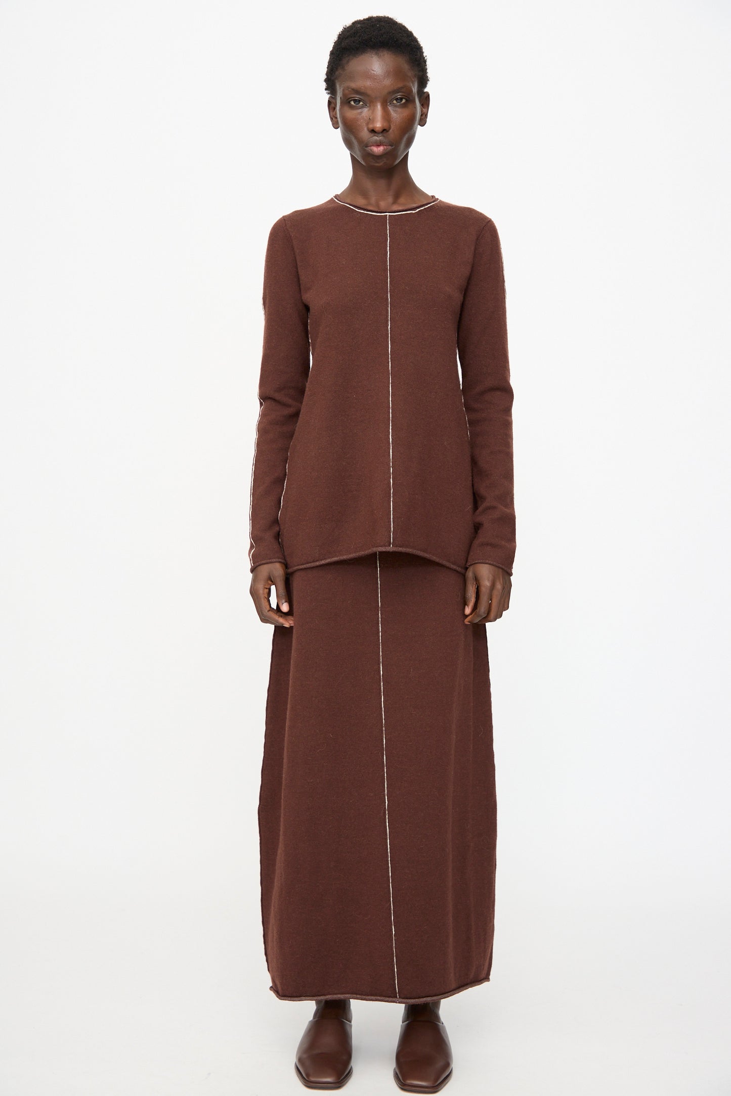 A woman faces forward against a white background wearing the Lauren Manoogian Stitch Skirt in Merlot, paired with a matching long-sleeved top and brown shoes. Visible center seams accentuate the coordinated look.